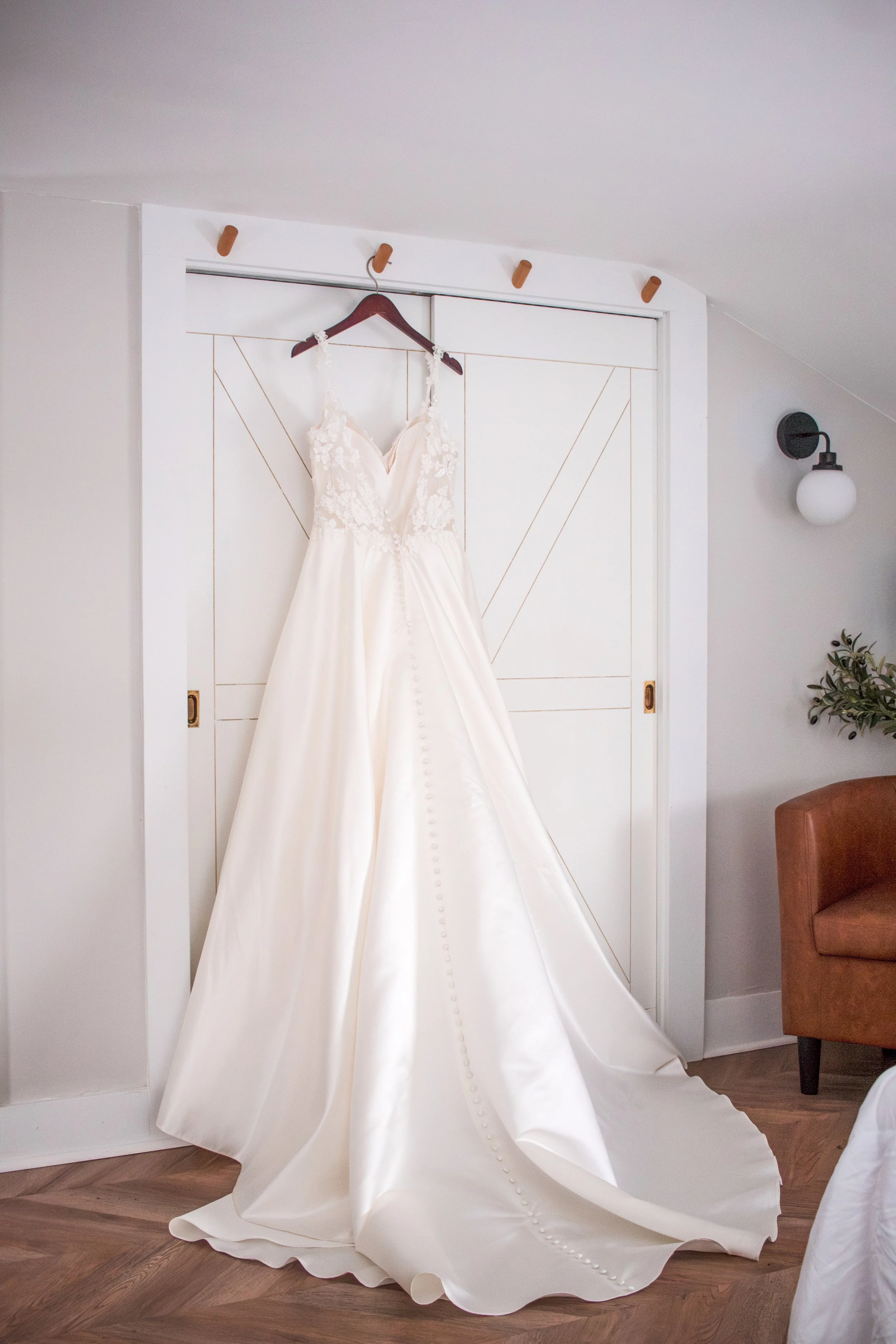 A wedding dress hanging on a dark wood hanger on a door.