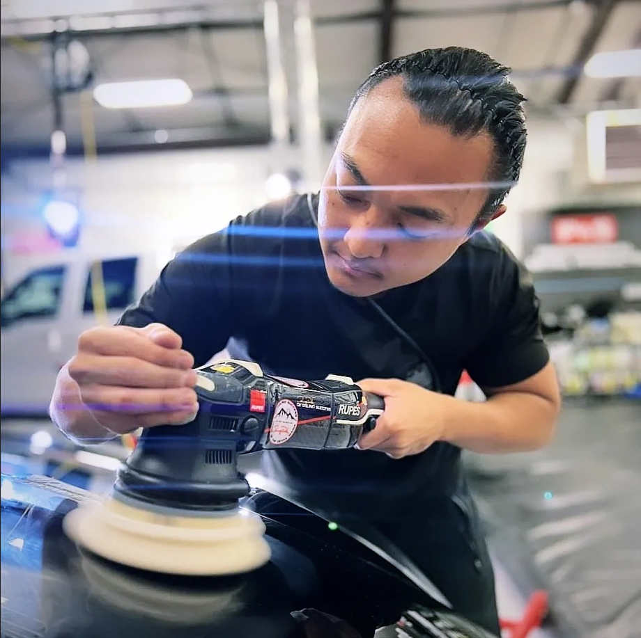 Detailer using an electric polisher on a black car in a garage