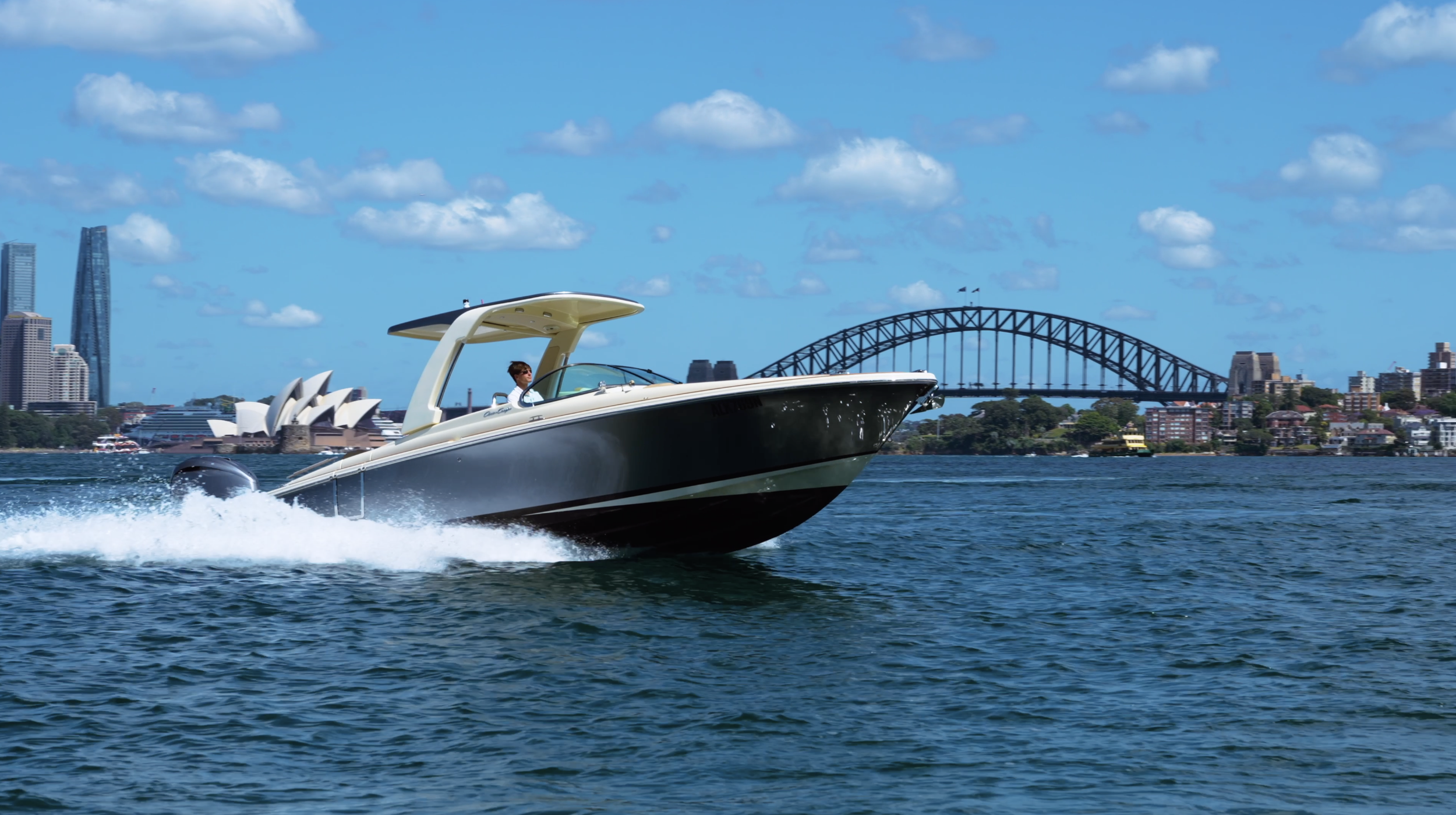 A boat speeding on the water with the Sydney Opera House and Harbour Bridge in the background on a bright, partly cloudy day.