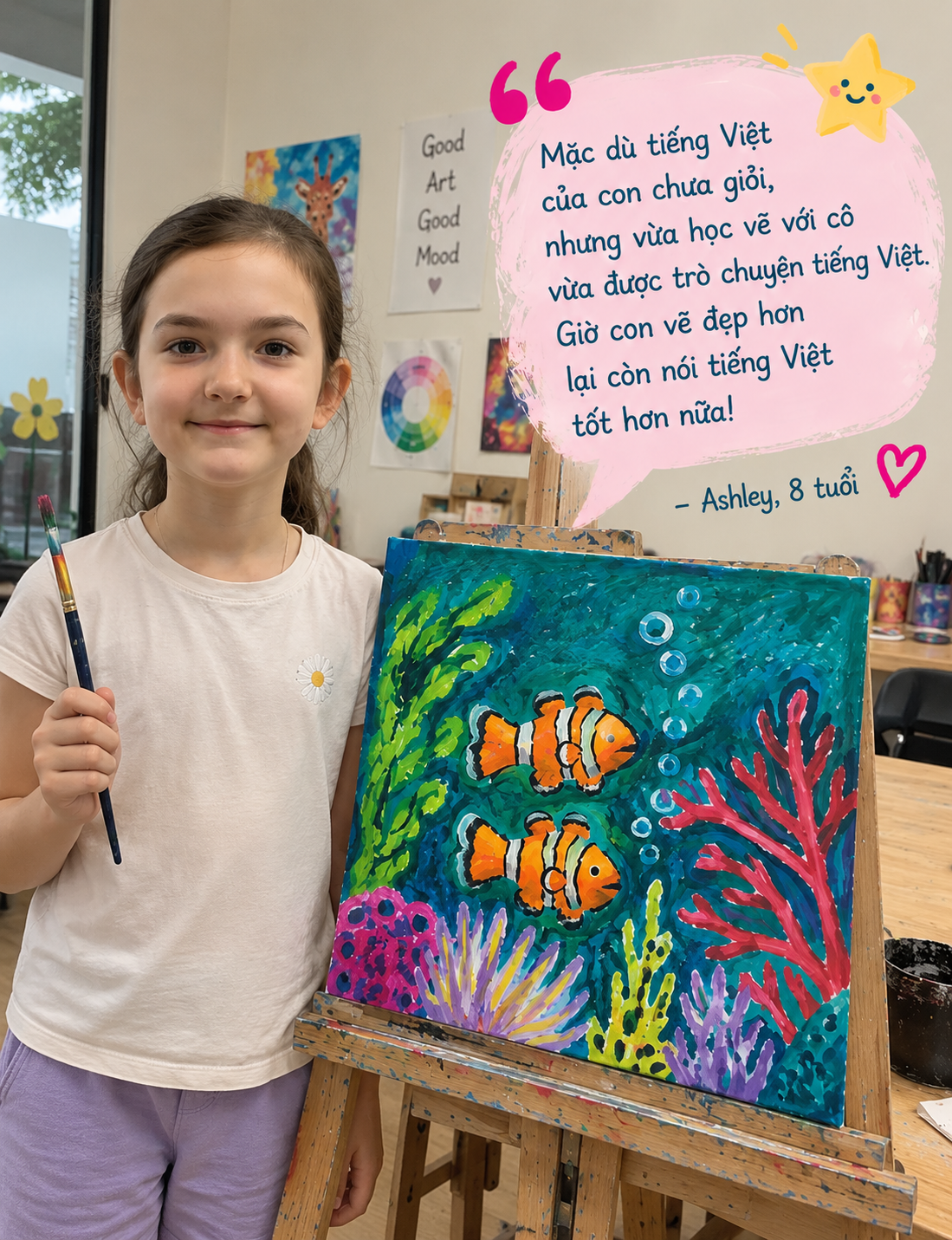 A young girl stands next to her vibrant painting of two orange clownfish and colorful underwater plants on a canvas. She holds a paintbrush and smiles at the camera in an art classroom, with various art supplies and colorful artwork on the walls behind her.