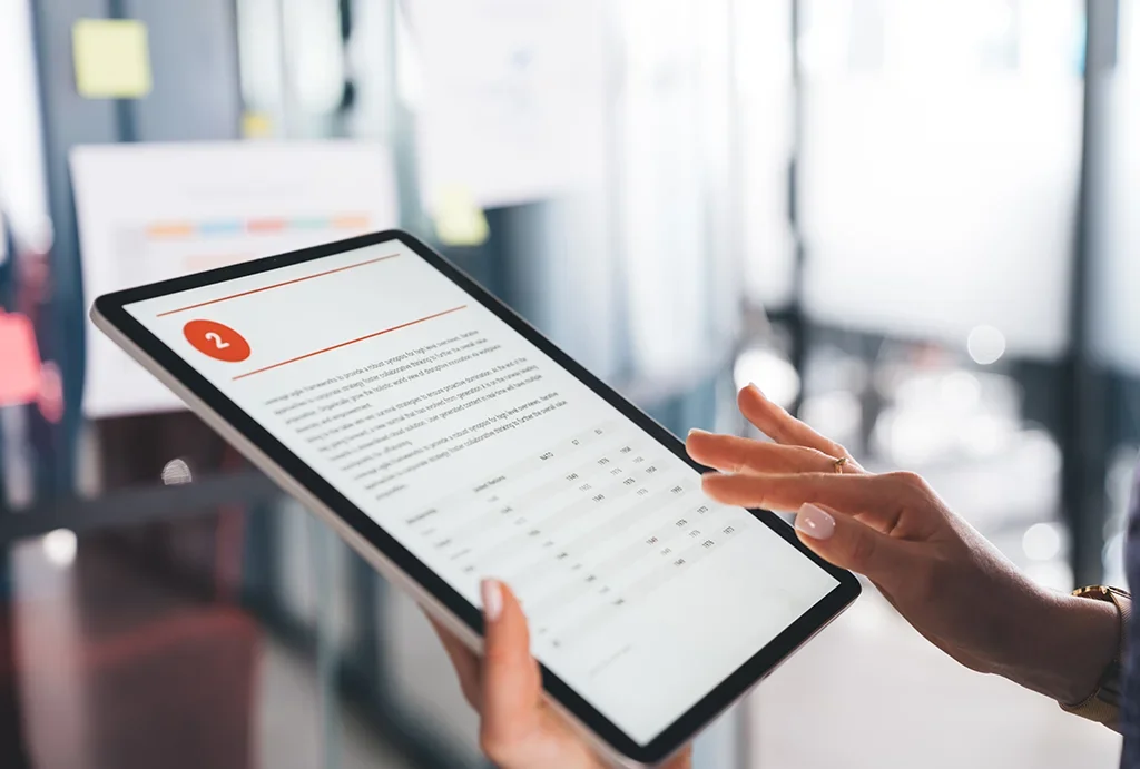 Person touching a tablet displaying a calendar and a to-do list in an office setting.