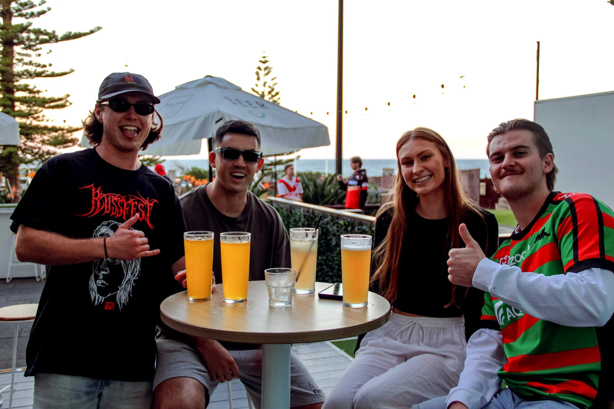 Two women serve draft beer at a bar, with labels on the taps reading Victoria Bitter, Tooheys New, Old, Hahn, Stone Wood Pacific Ale, and Carlton Dry. The women are smiling and pouring beers into glasses.