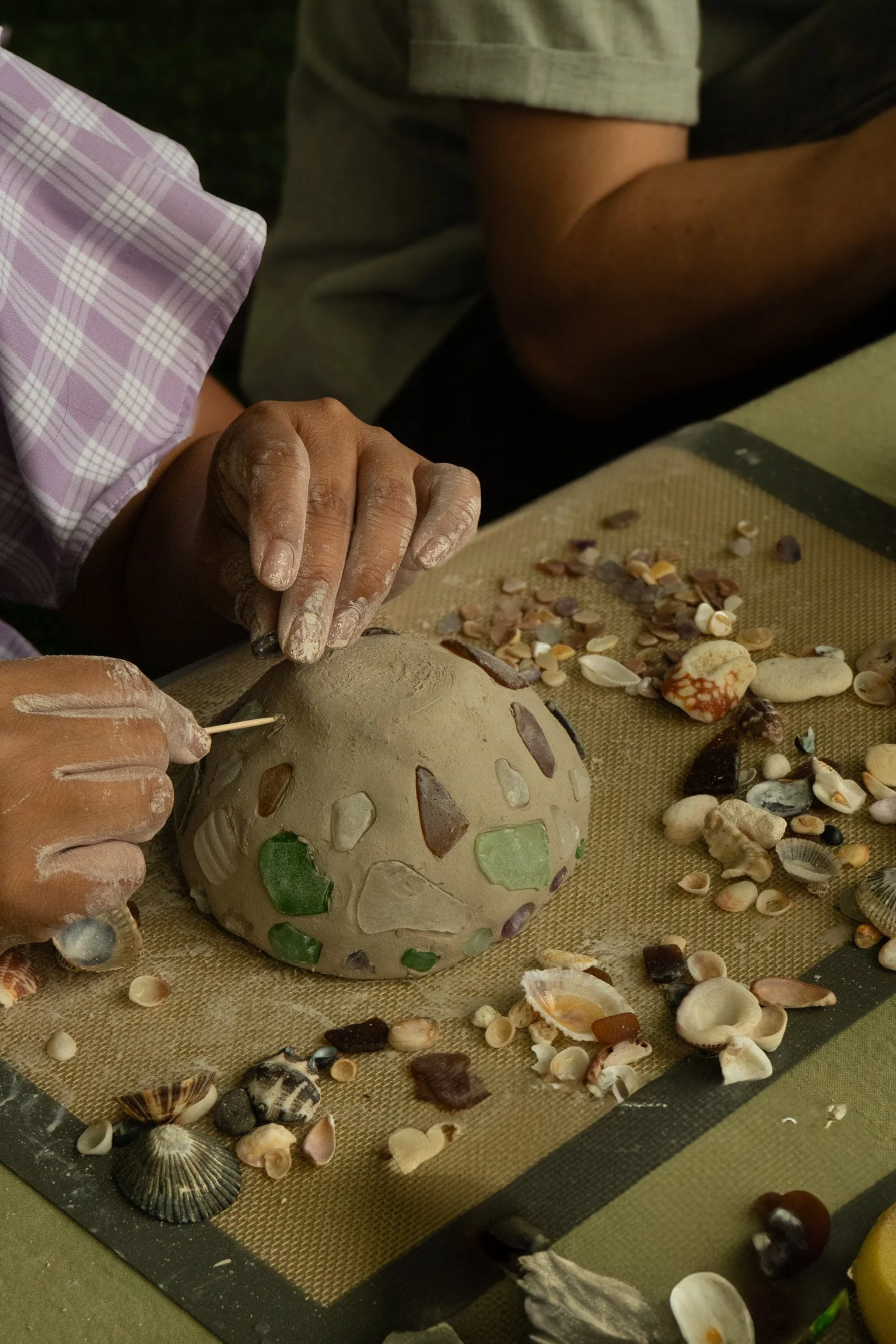 Person working on a decorative mosaic globe surrounded by seashells and stones.