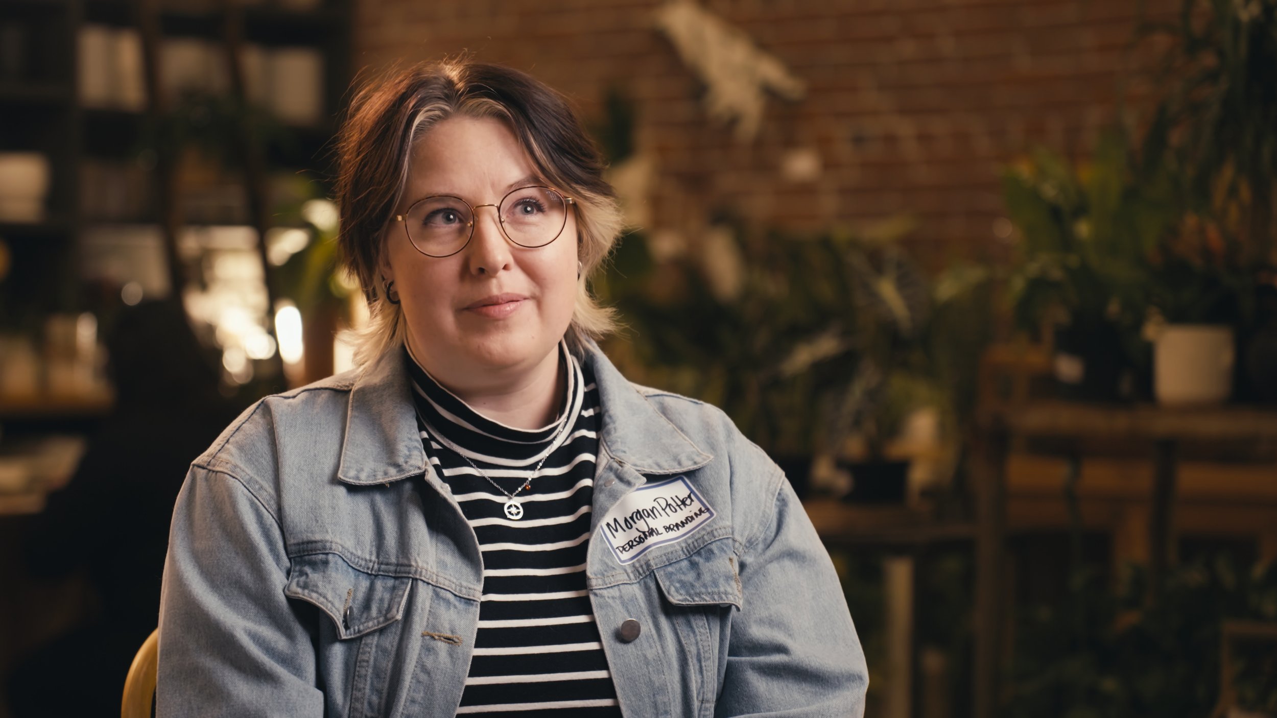 Person wearing glasses and a denim jacket, sitting indoors with plants and a brick wall in the background — captured in a high-quality Sacramento video.