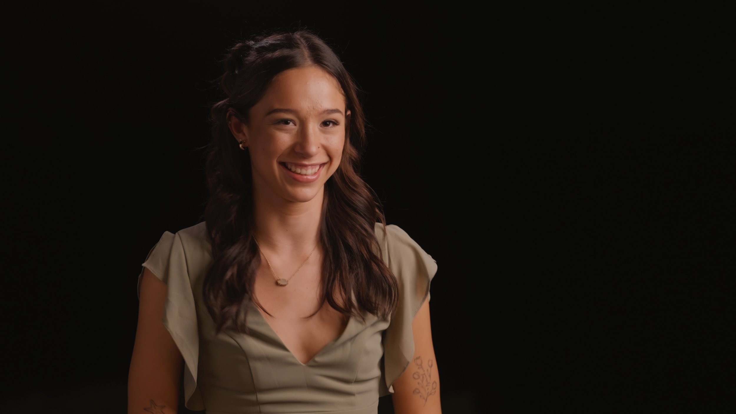Bride’s sister smiling, with a tattoo and necklace, against a black background — captured in a high-quality Sacramento wedding video.