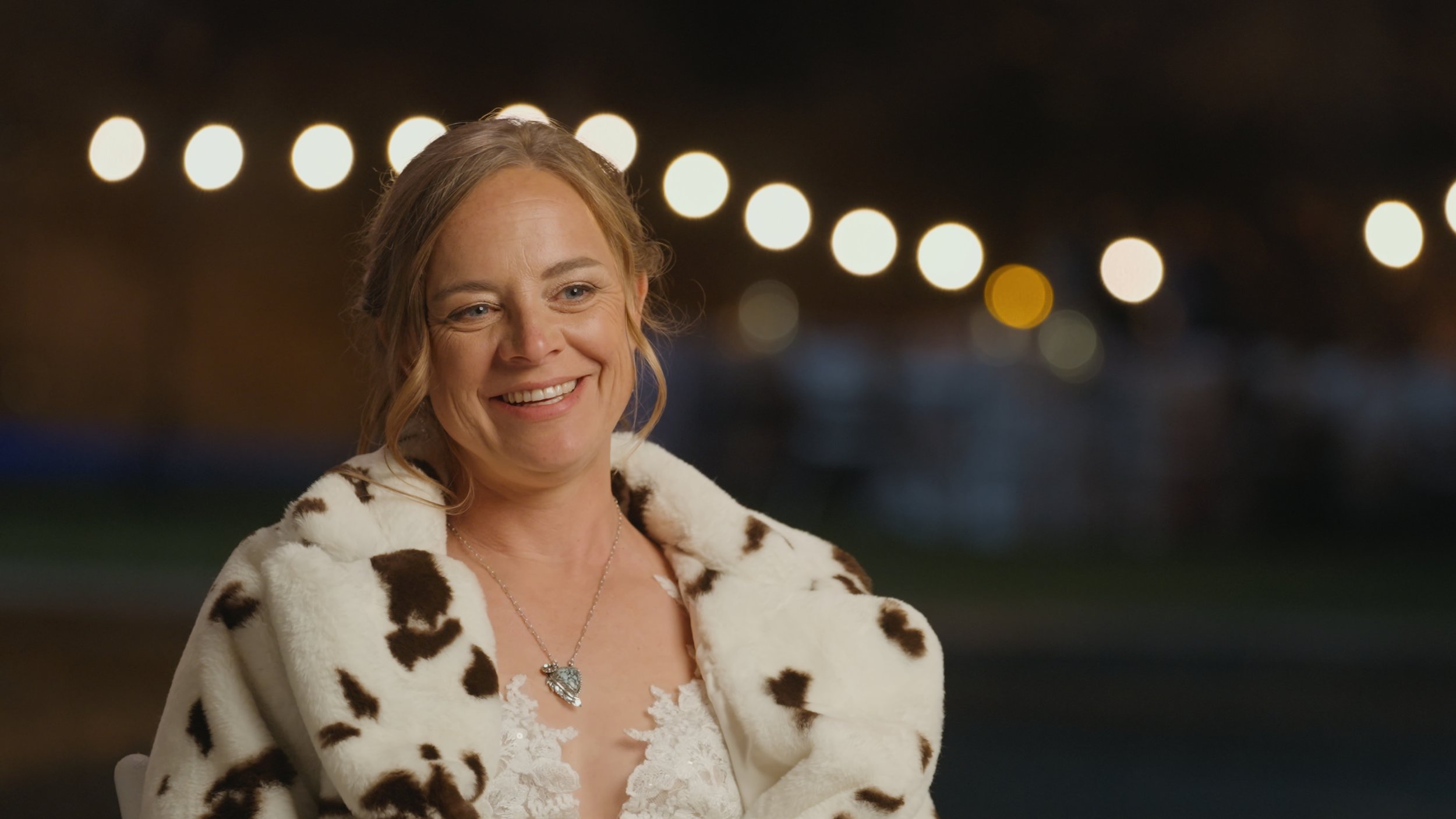 Bride, woman smiling in a cow print coat with string lights in the background — captured in a high-quality Sacramento wedding video.