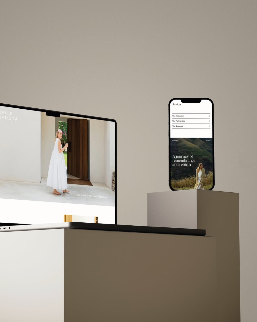 A computer and a smartphone on pedestals displaying minimalist mobile and desktop website designs featuring women in white dresses outdoors.