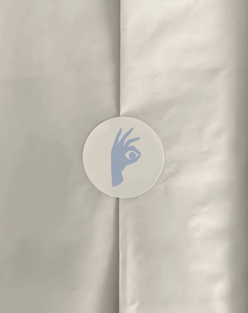 A circular sticker with a stylized blue hand forming an eye shape, attached to the white paper surface.