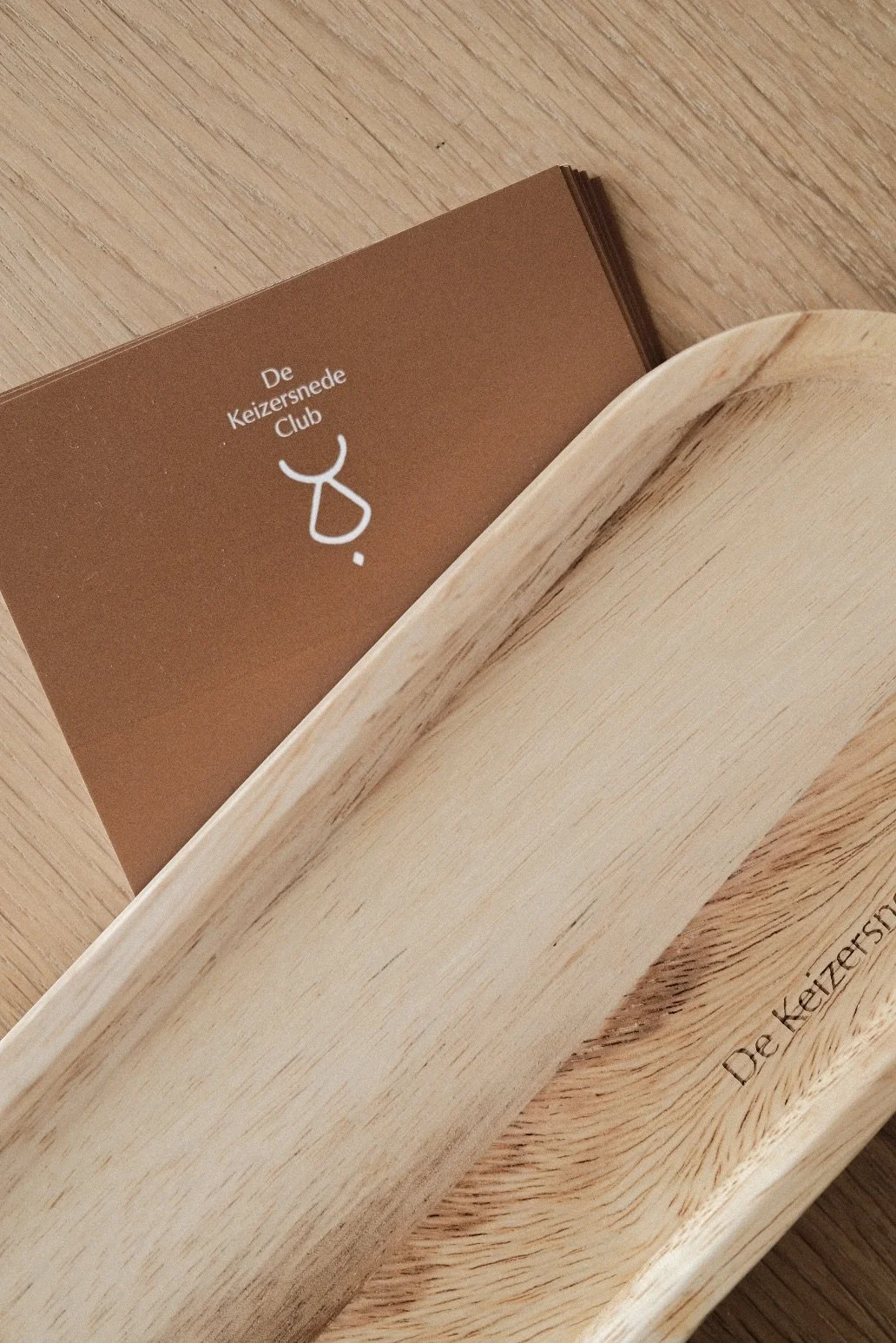 A brown booklet inside a light-colored wooden box, with the text "De Keizersnede Club" and a symbol on the cover.