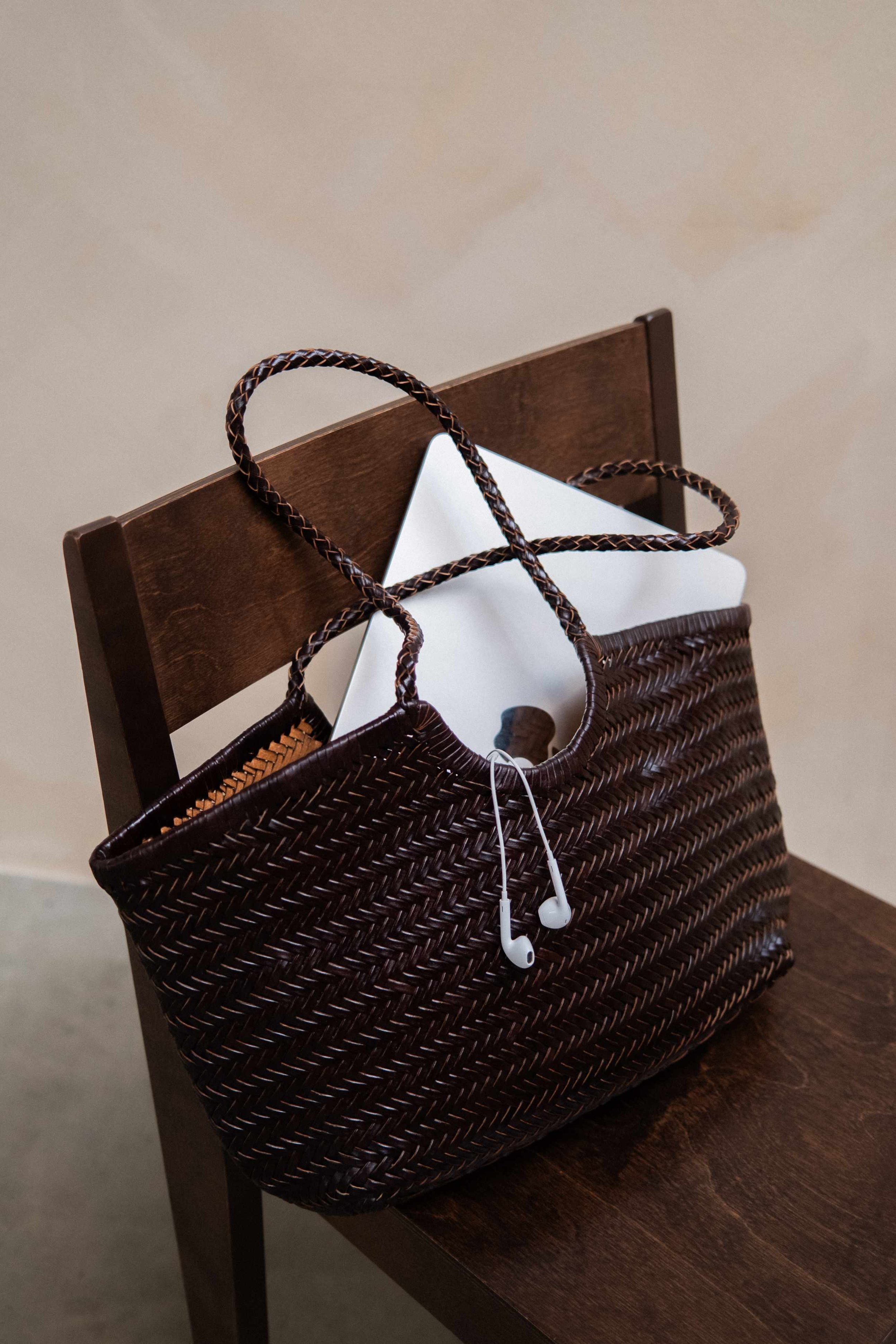 Wicker basket, white electronic device, and white earphones on a wooden chair with a dark finish.