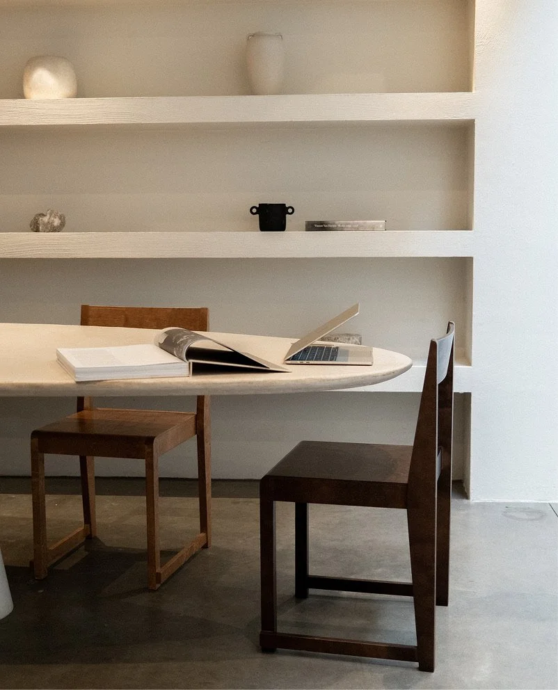 A room with a white round table, two wooden chairs, and built-in white shelves with decorative items and books.