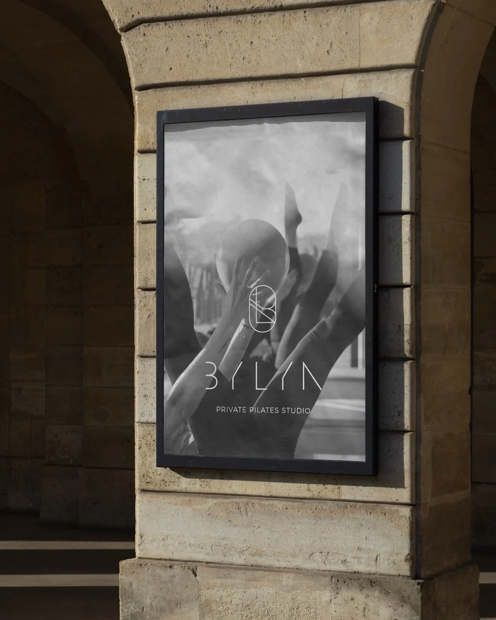 Black and white poster for a private Pilates studio called '3YLIN', featuring a person holding a Pilates ball with raised hands, mounted on a brick wall.