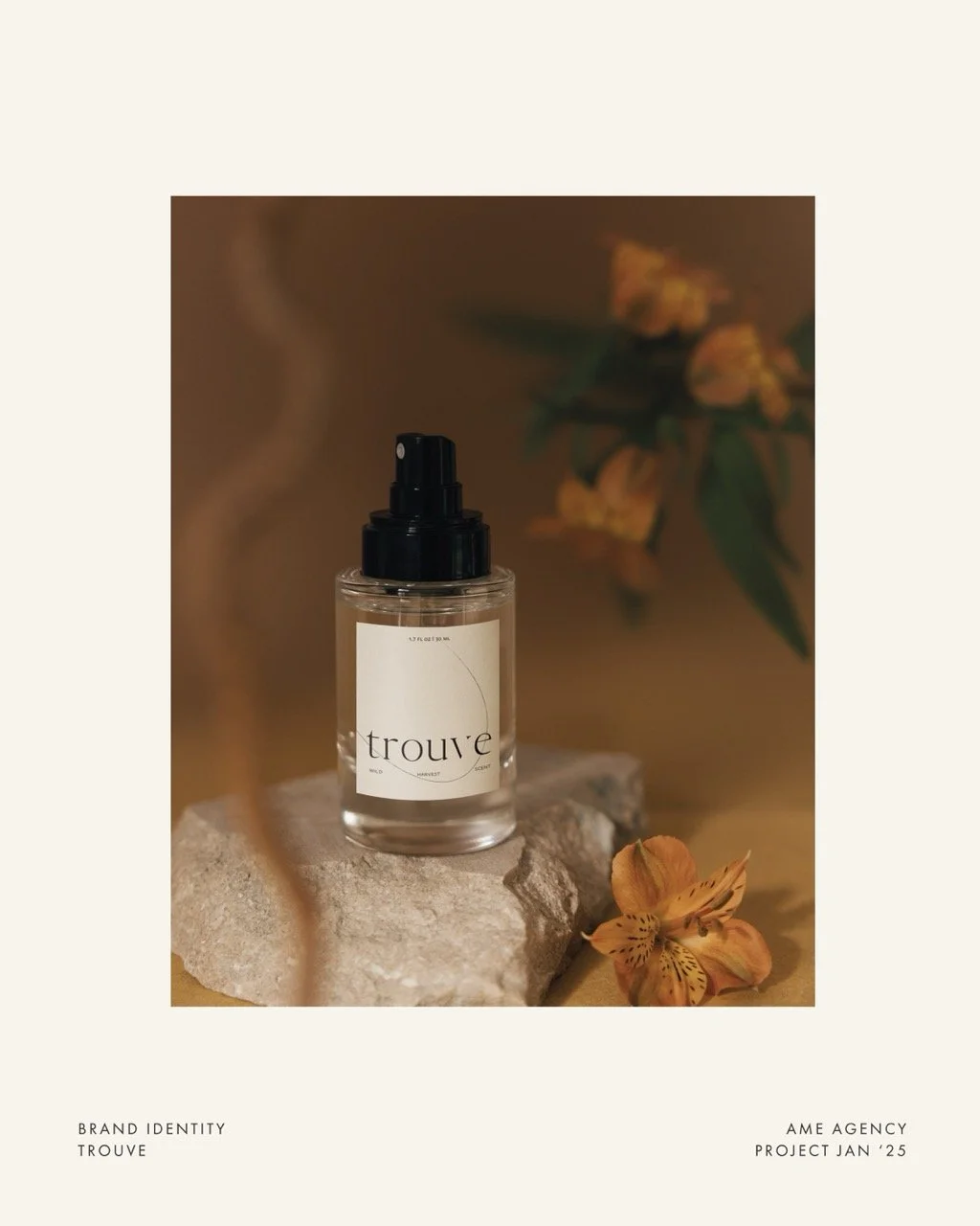 A small clear spray bottle labeled 'trouve' with a black spray nozzle, placed on a stone, surrounded by orange and yellow flowers, with blurred floral background.