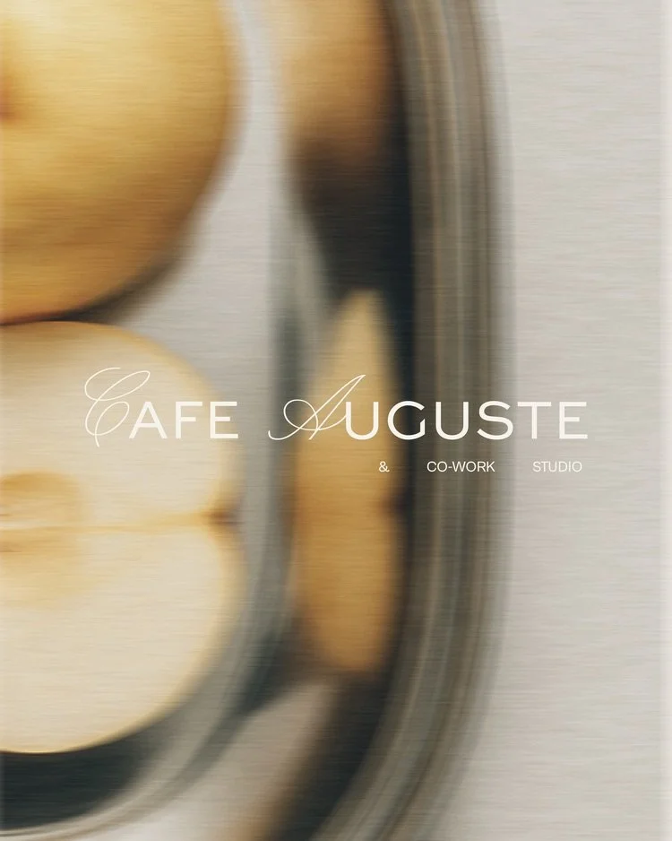Blurred close-up of a coffee cup or saucer with the text 'Café Auguste & Co-Work Studio' overlayed.