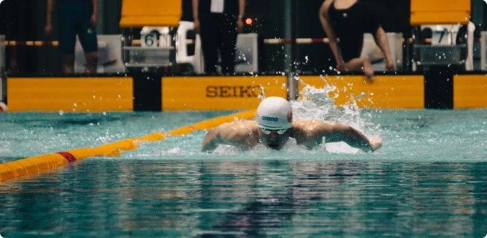 Swimmer competing in a swimming race, emerging from the water after a stroke, in a pool at a competitive event.