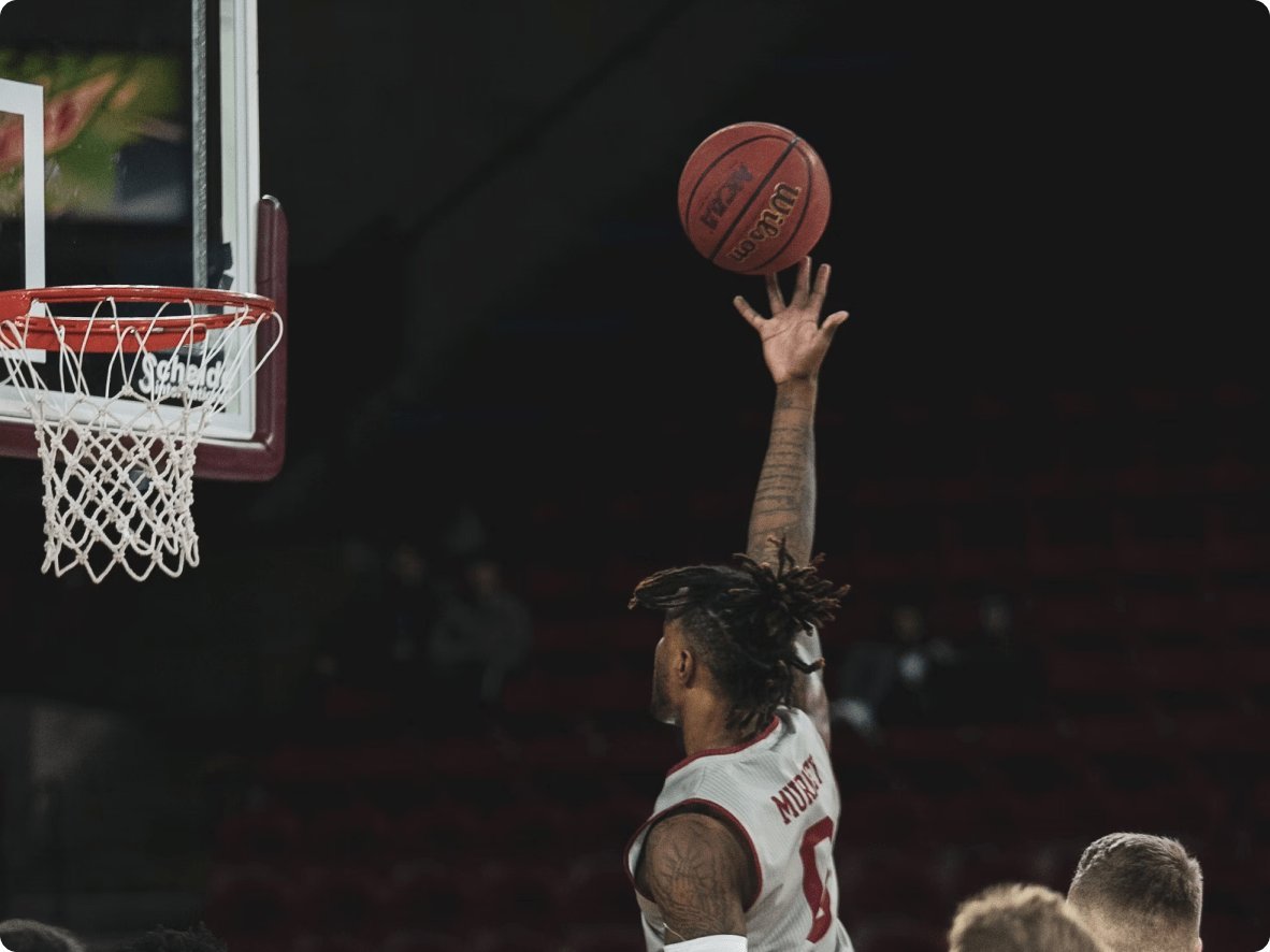 A basketball player in a white jersey with red accents, number 0, leaps towards the hoop for a dunk, with his right arm extended and the basketball in his hand.