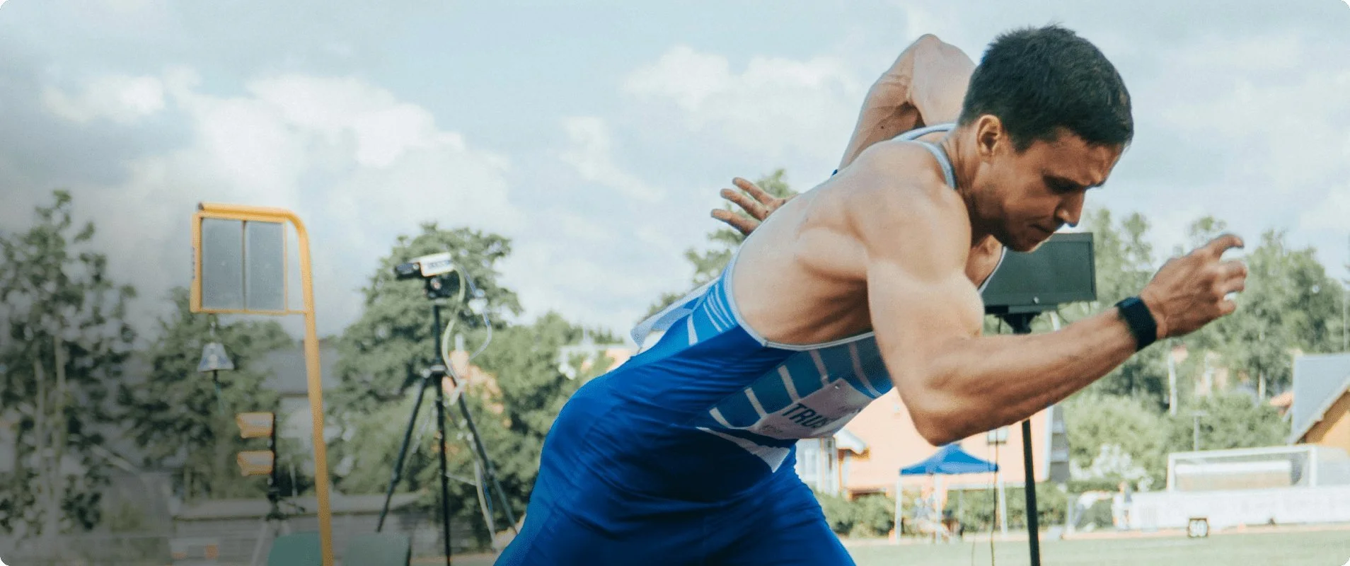 Male athlete in blue running gear begins a sprint at a track meet during daytime.