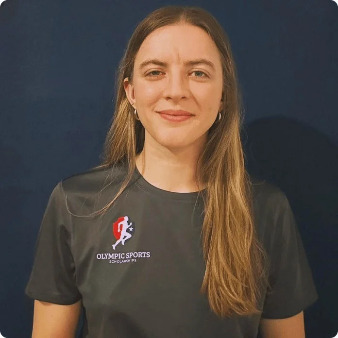 Young woman with long brown hair wearing a black t-shirt with 'Olympic Sports Scholarships' logo, standing against a dark blue background.