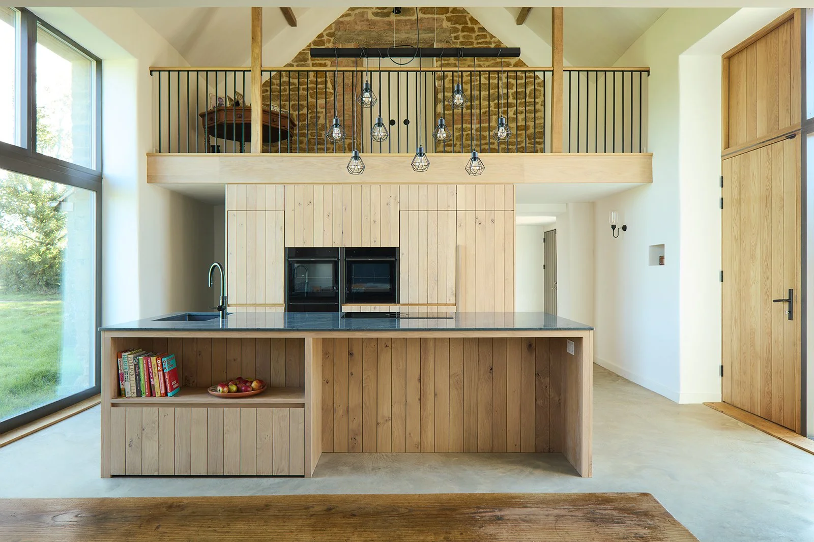 Taw Fitzwilliam Ltd — Barn conversion showing modern oak kitchen, large sliding glass door, reinstated original barn openings and an open loft with black metal railing. Han