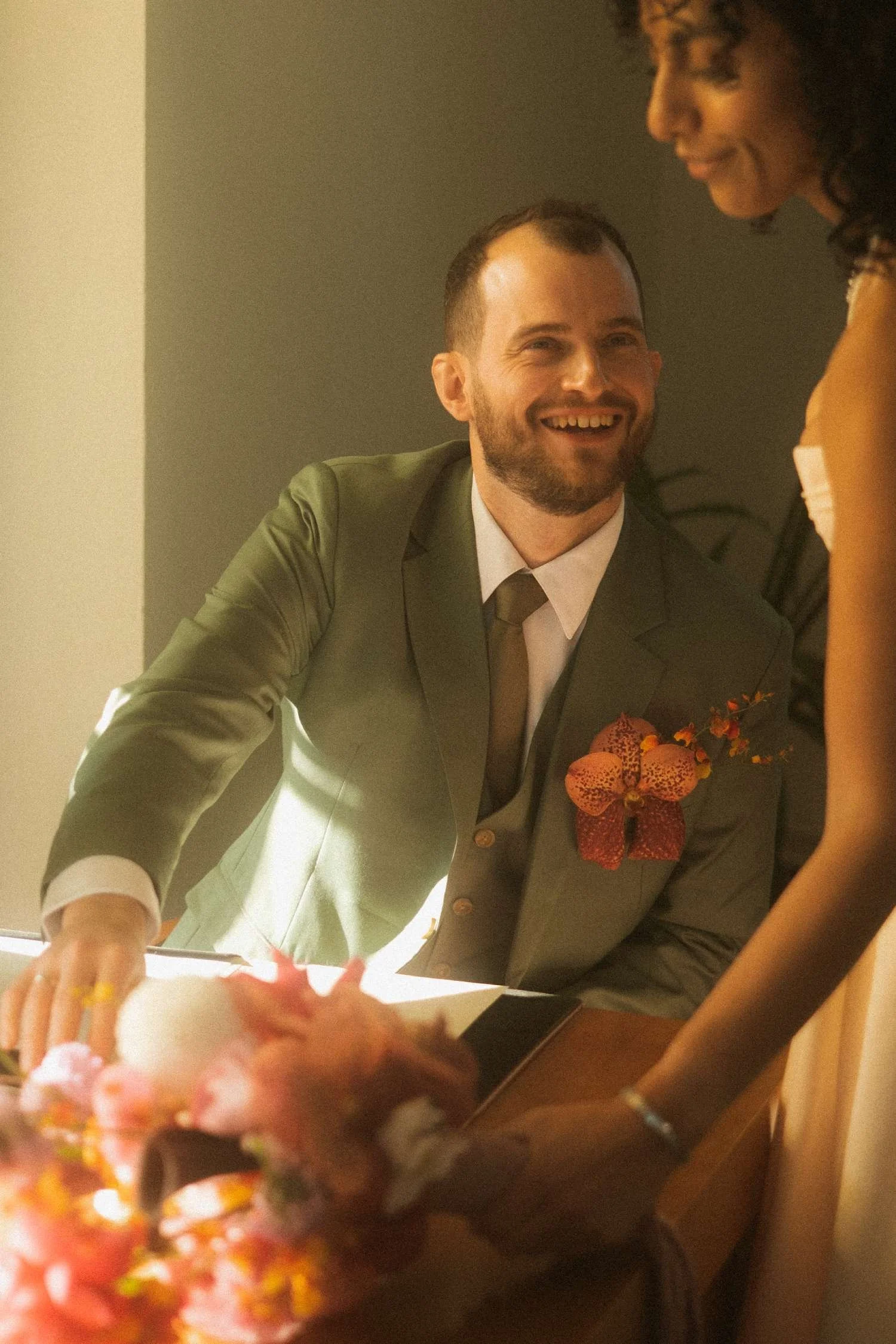 Groom smiling warmly at the bride while standing beside the desk during the marriage register signing.