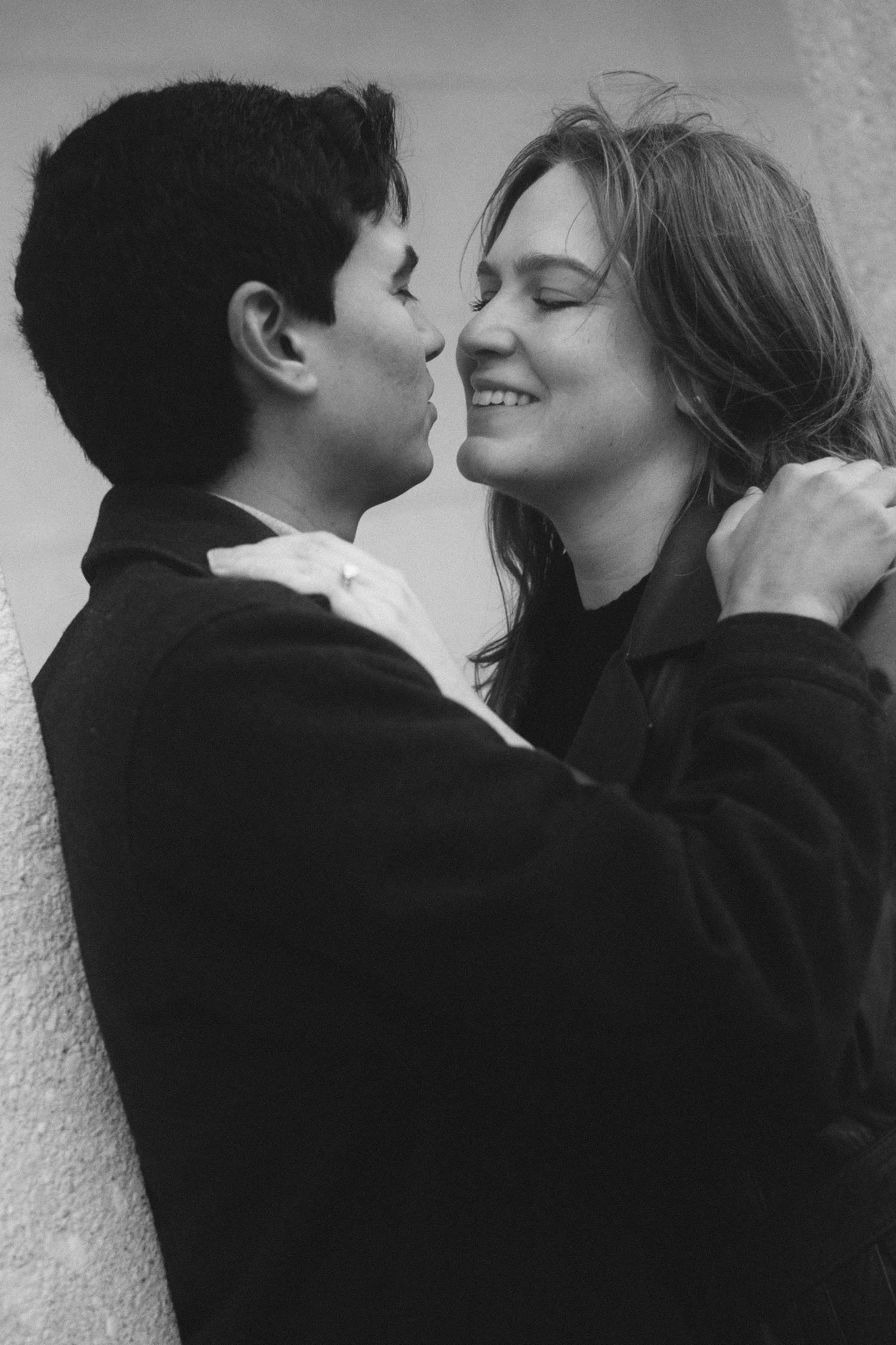 Smiling couple standing close together against a stone wall in this black and white Berlin engagement photo