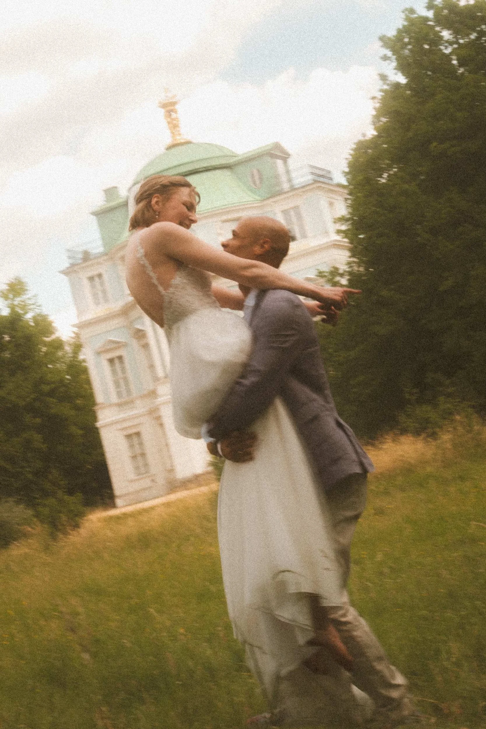 Groom lifting bride high in meadow with Schloss Charlottenburg Belvedere pavilion clearly visible, Berlin