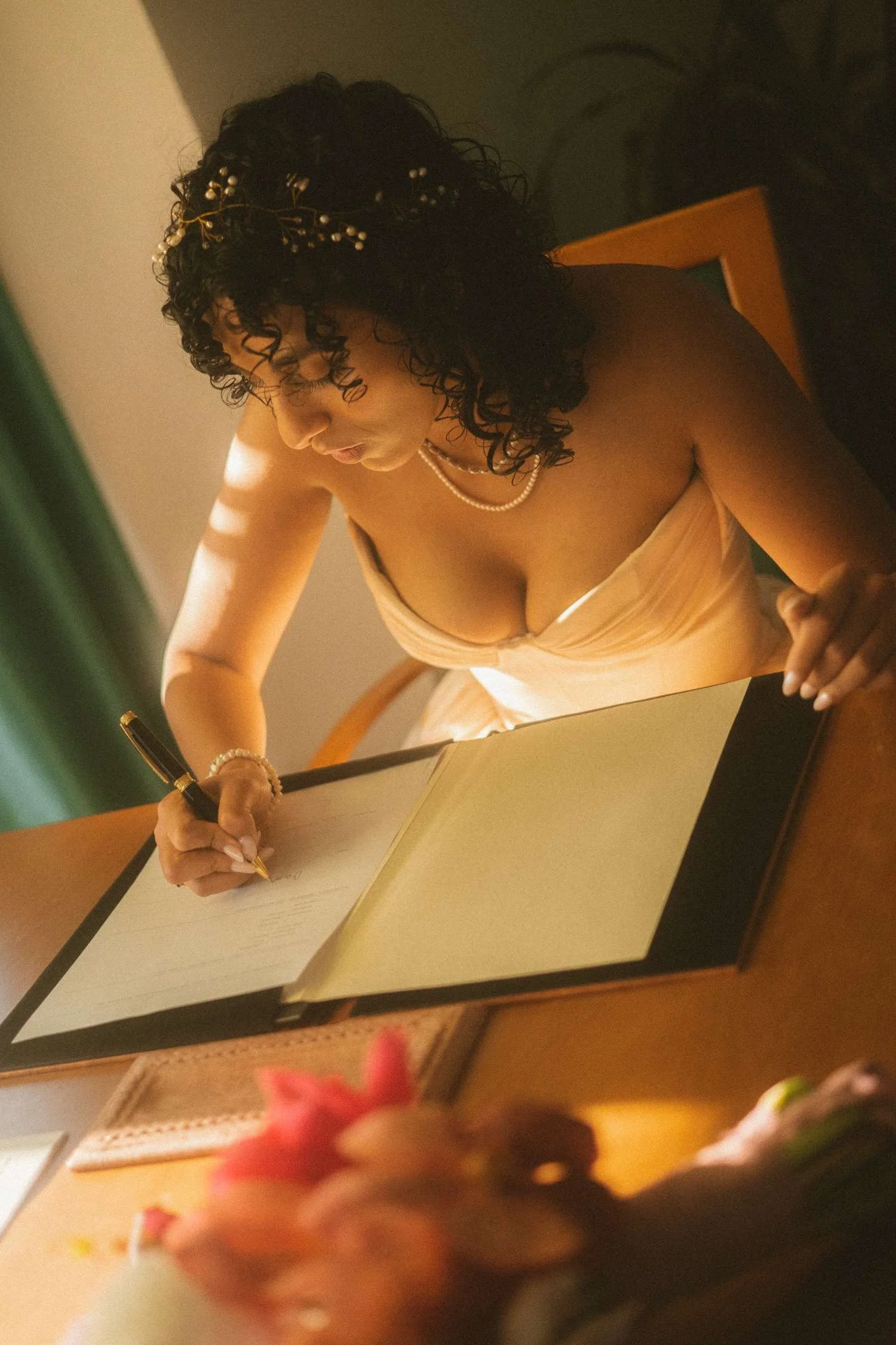 Close-up of the bride signing the marriage register at a desk during a civil wedding ceremony, captured in warm natural light.
