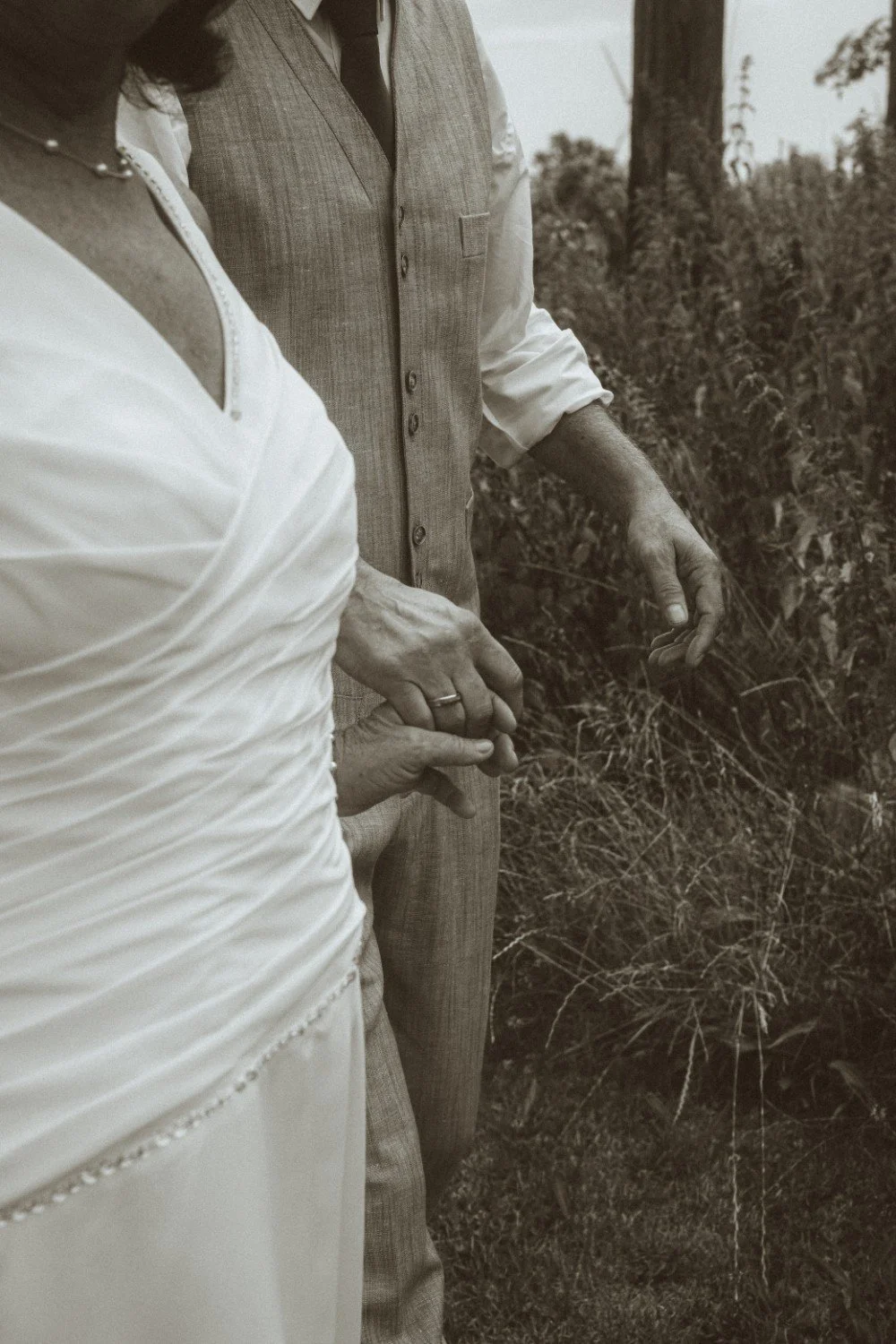 A close-up black and white outdoor shot of the wedding couple walking together and holding hands.