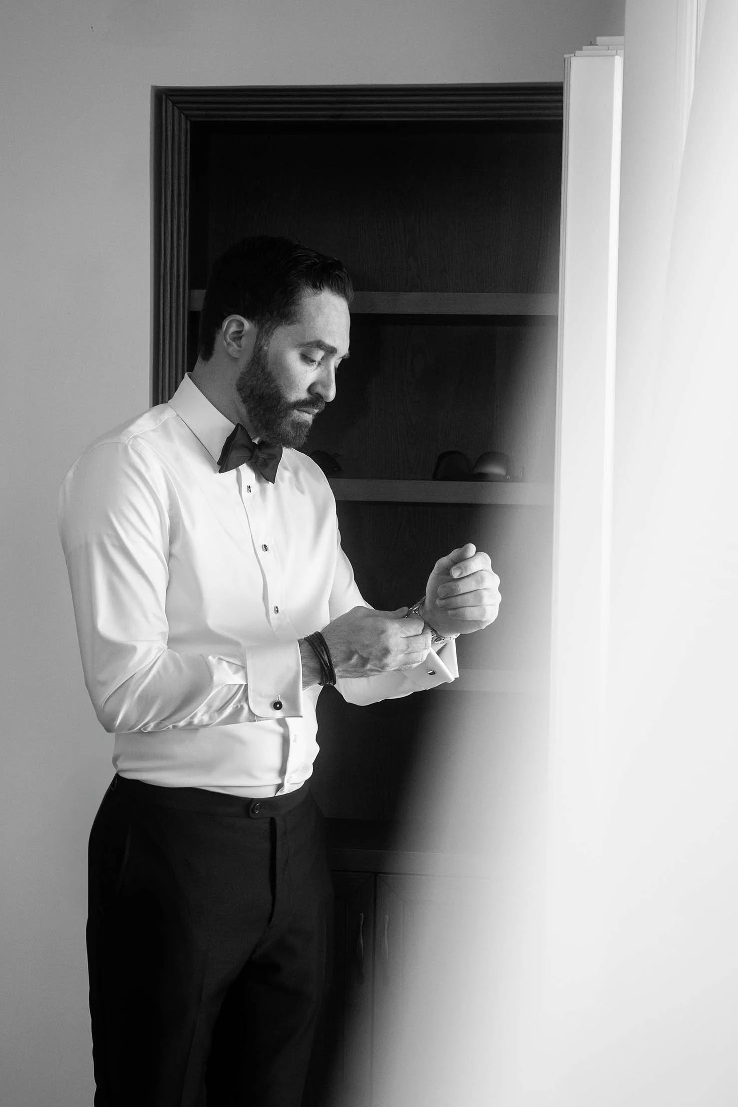 Groom adjusting his cufflinks during wedding morning preparations in Sicily, quiet black and white portrait.