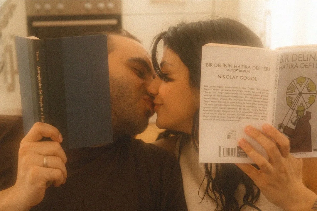 Candid portrait of a couple kissing while holding books in their Berlin Kreuzberg apartment with warm, cinematic lighting.