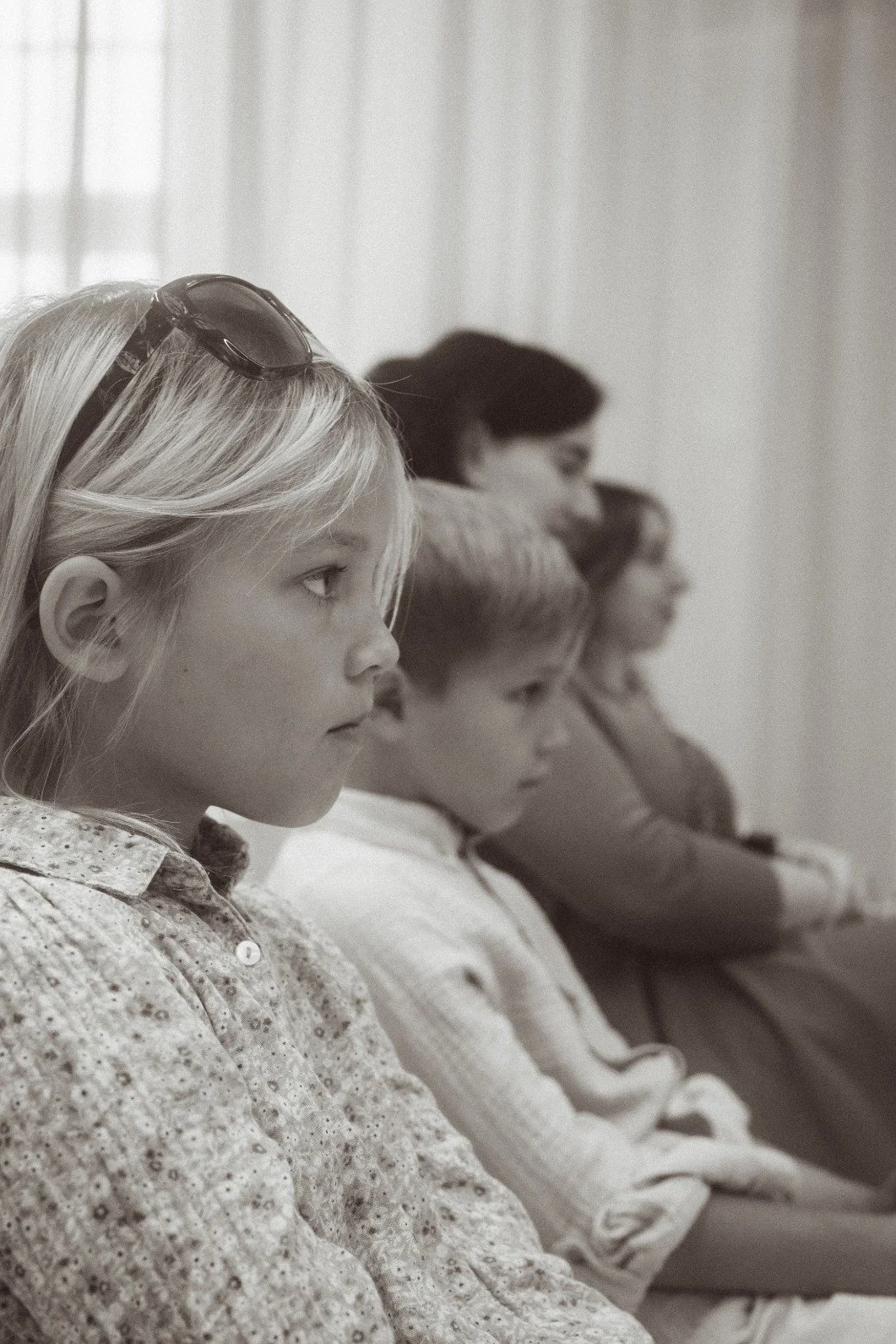 A black and white portrait of wedding guests, including children and women, seated together during an indoor ceremony.