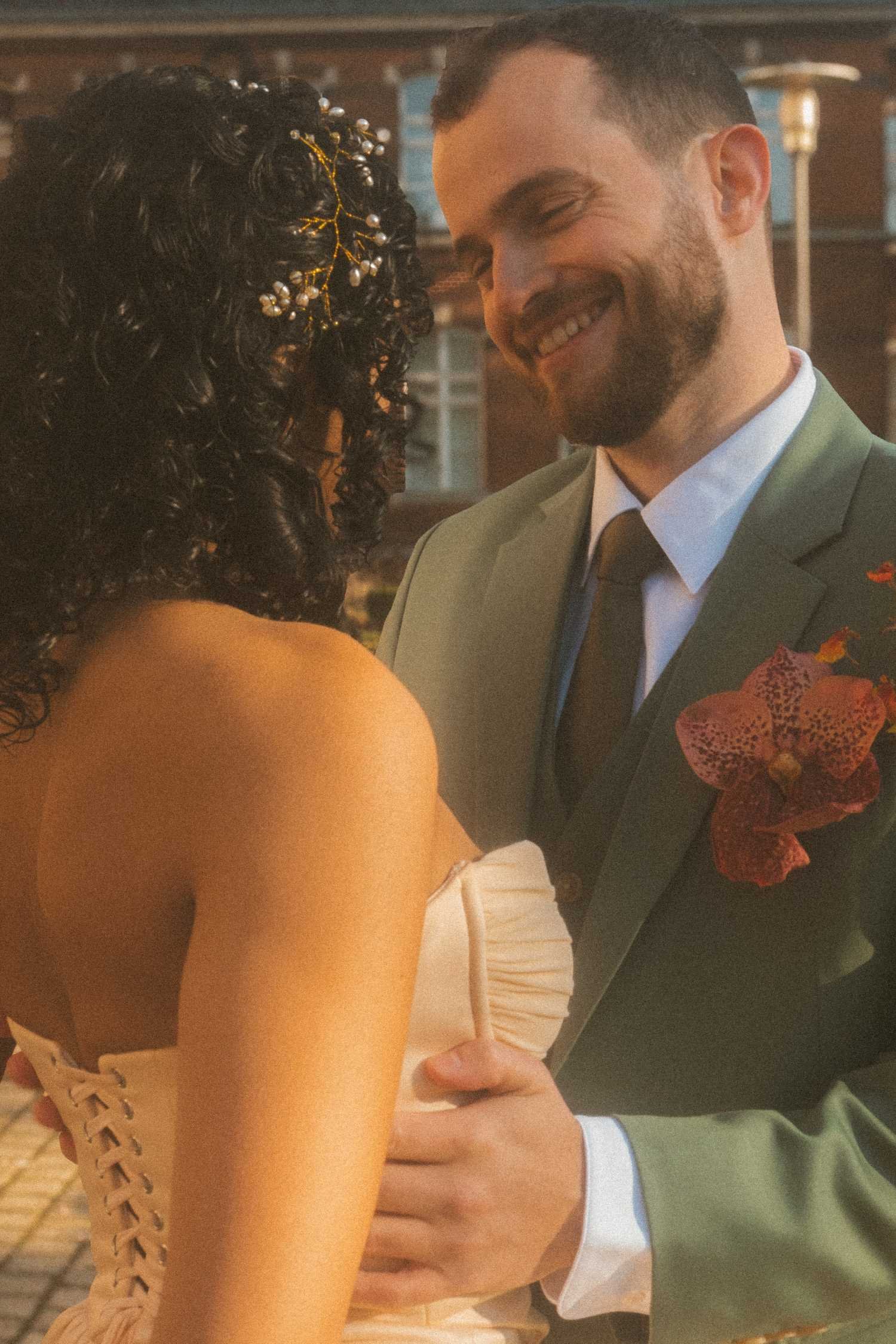 Groom smiling softly at the bride during an intimate outdoor wedding portrait, with hands resting gently at her waist.