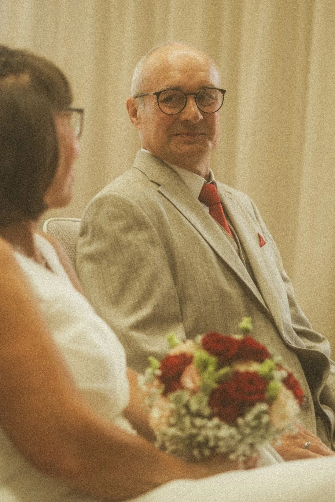 A close-up portrait of a smiling groom in a suit looking at the bride during their wedding ceremony.