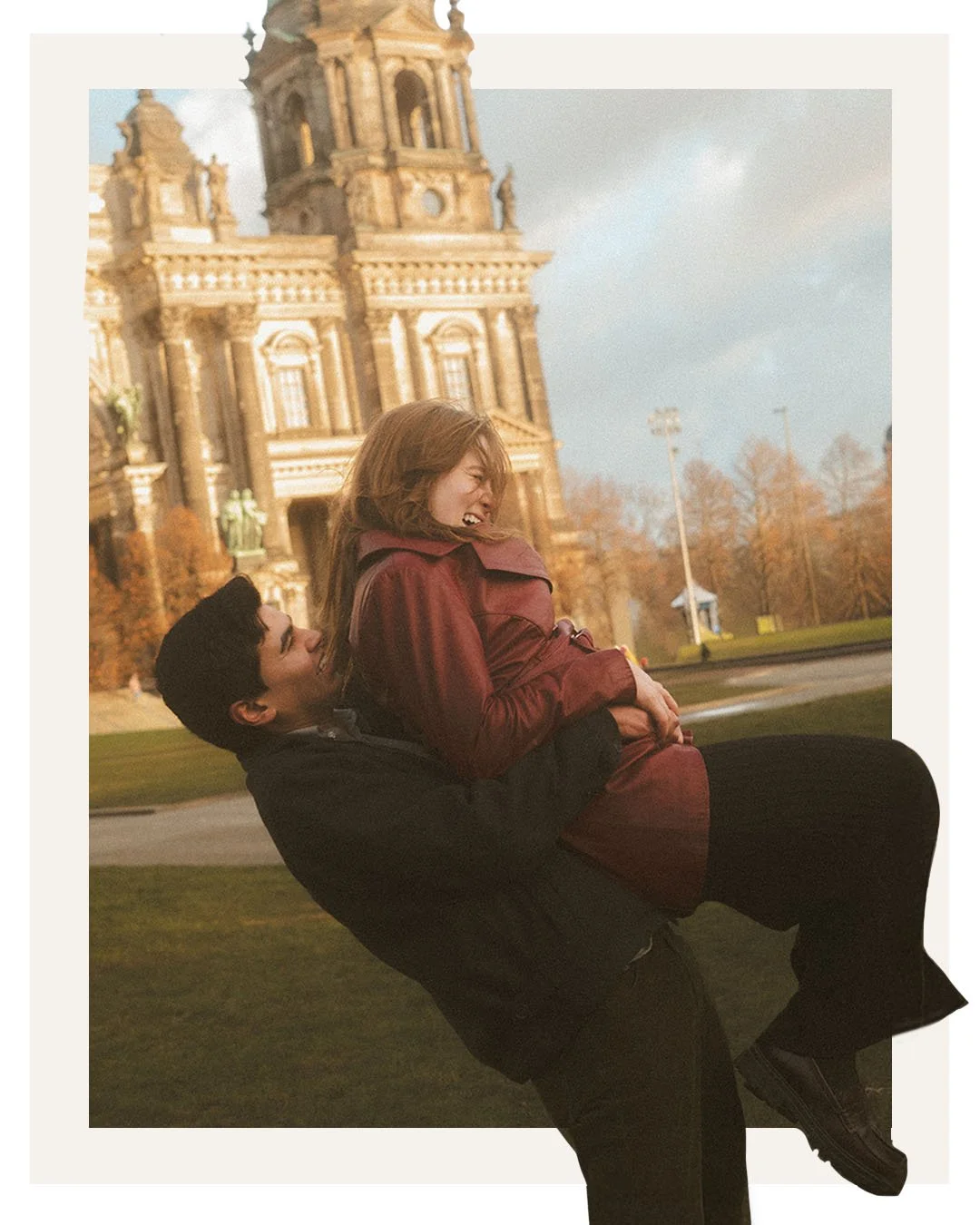 Playful couple laughing as the man lifts his partner in front of Berlin Cathedral during an engagement photoshoot in Berlin