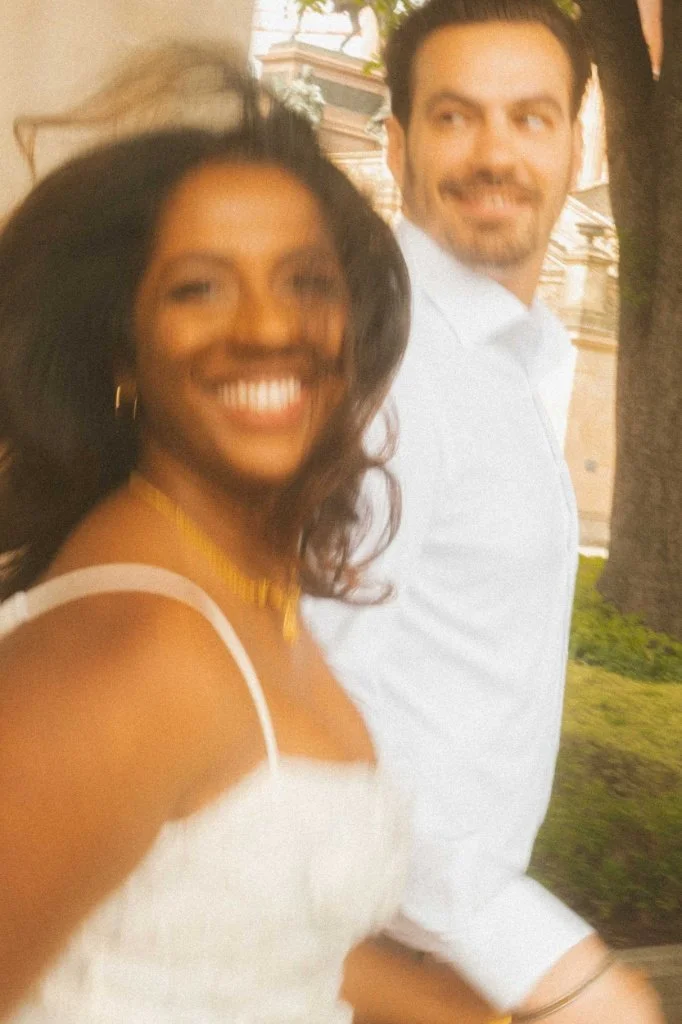 A joyful couple running together during a sun-drenched engagement photoshoot in Berlin, capturing candid laughter and movement.