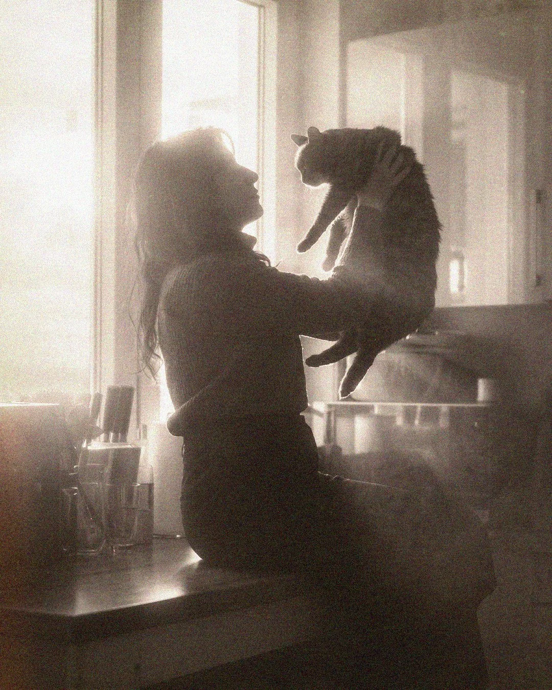 Grainy silhouette of a woman holding her cat by a window in a Berlin apartment with soft cinematic light.
