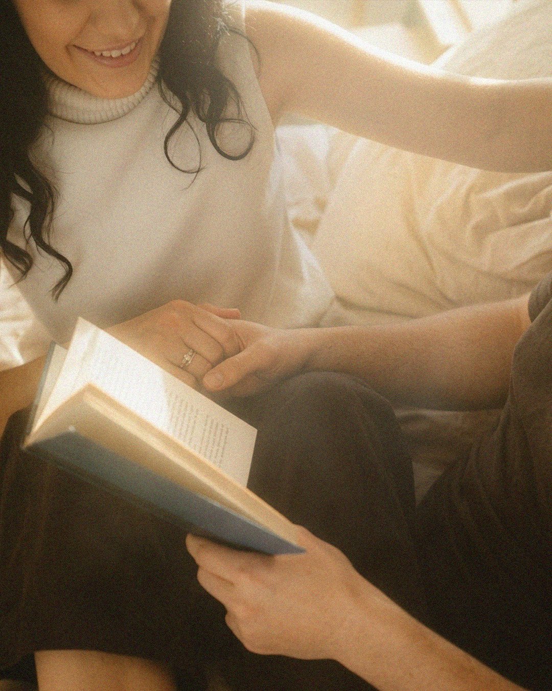 Close-up lifestyle portrait of a couple holding hands while reading a book together in a sunlit Berlin Kreuzberg apartment.