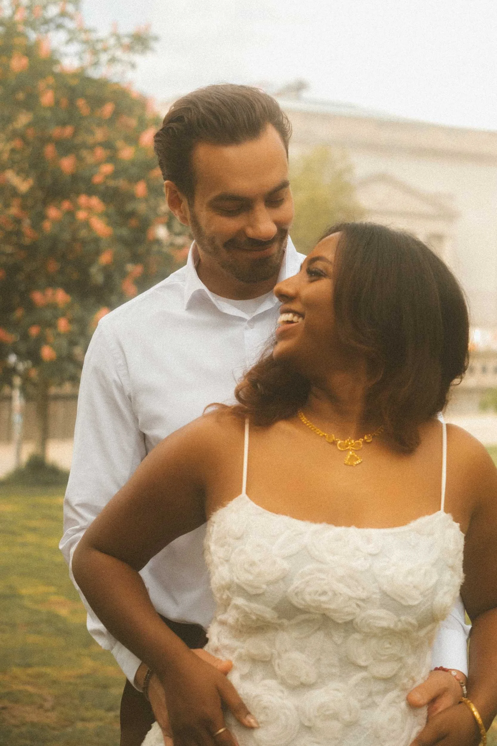 An engagement portrait in Berlin featuring the groom embracing the bride from behind and looking down at her with a smile, as she gazes to the side with a smile.