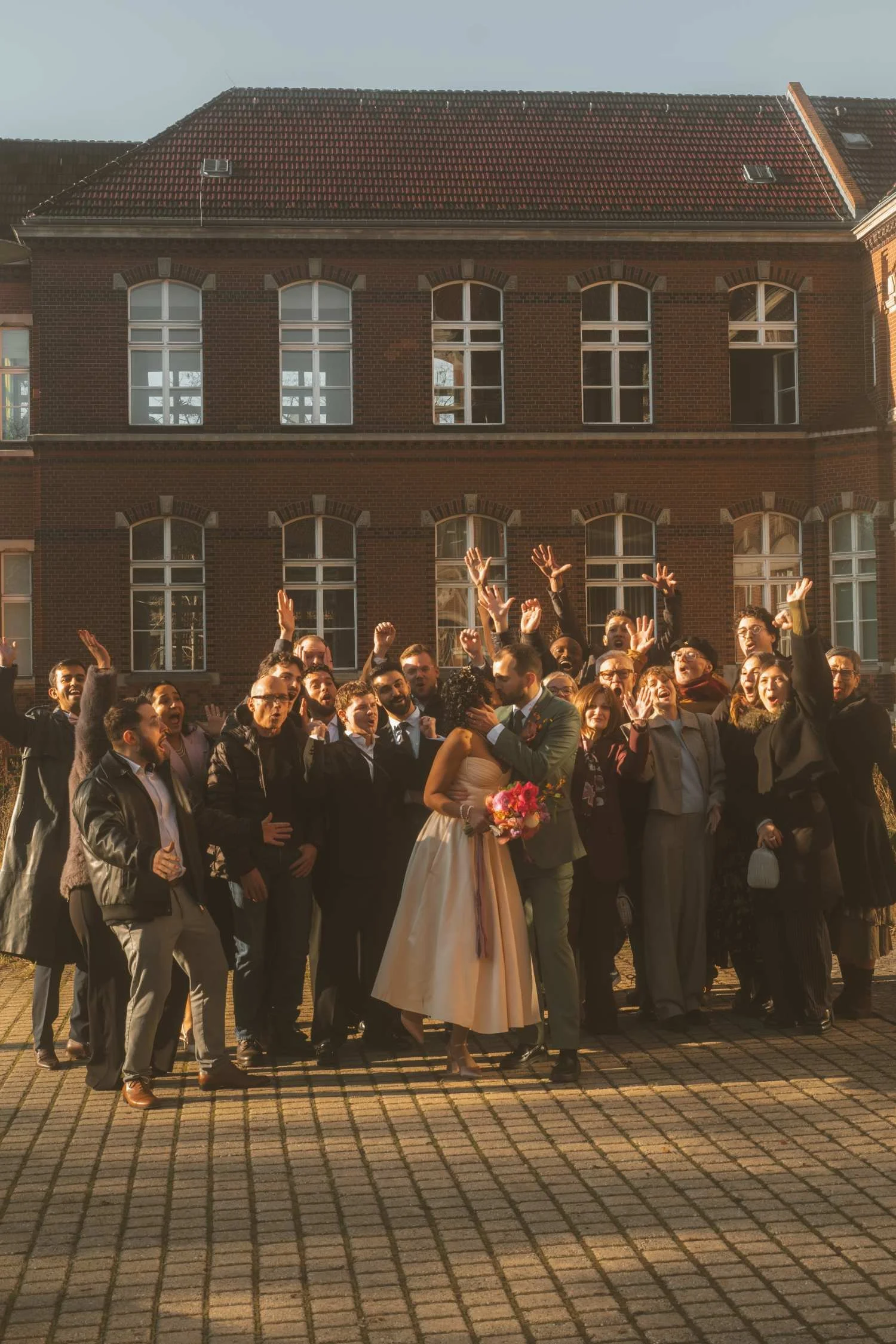 Bride and groom standing together in front of a cheering group of guests outside the civil registry office, celebrating the wedding day.