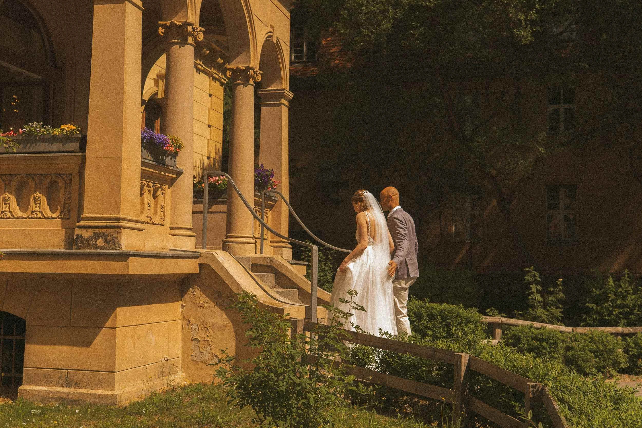 Couple from behind walking toward ornate historic Berlin Standesamt building surrounded by summer gardens