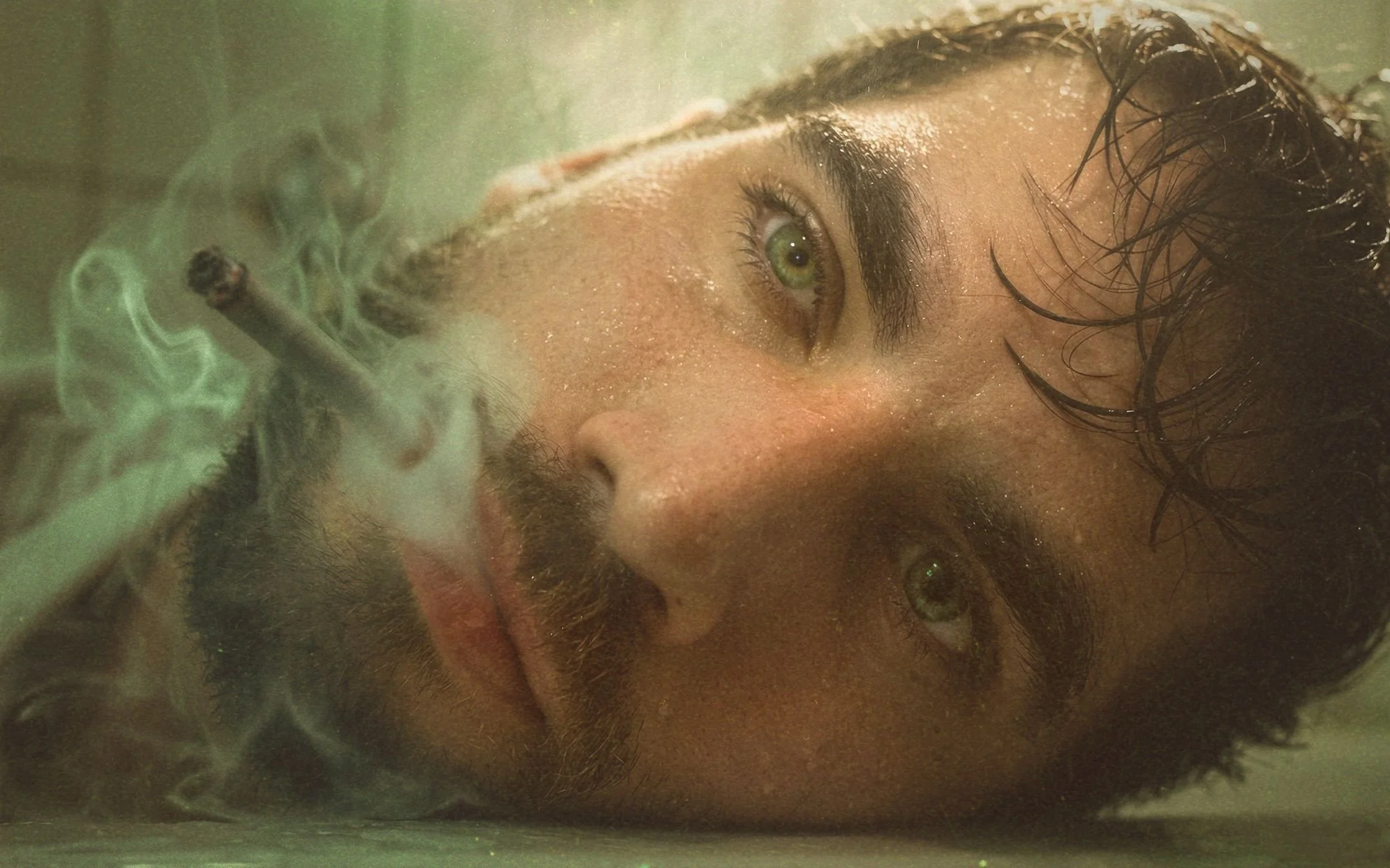 Close-up cinematic portrait of man with green eyes smoking in bathtub, moody storytelling photography in Berlin