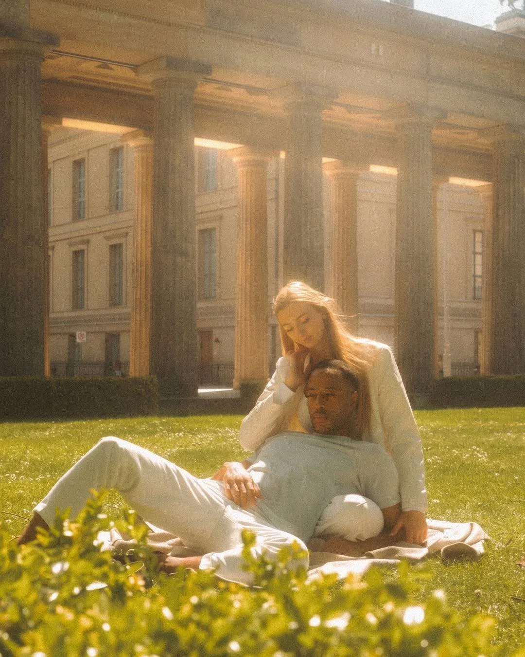 A couple relaxing on a blanket on the grass in front of historic sunlit stone columns in Berlin.
