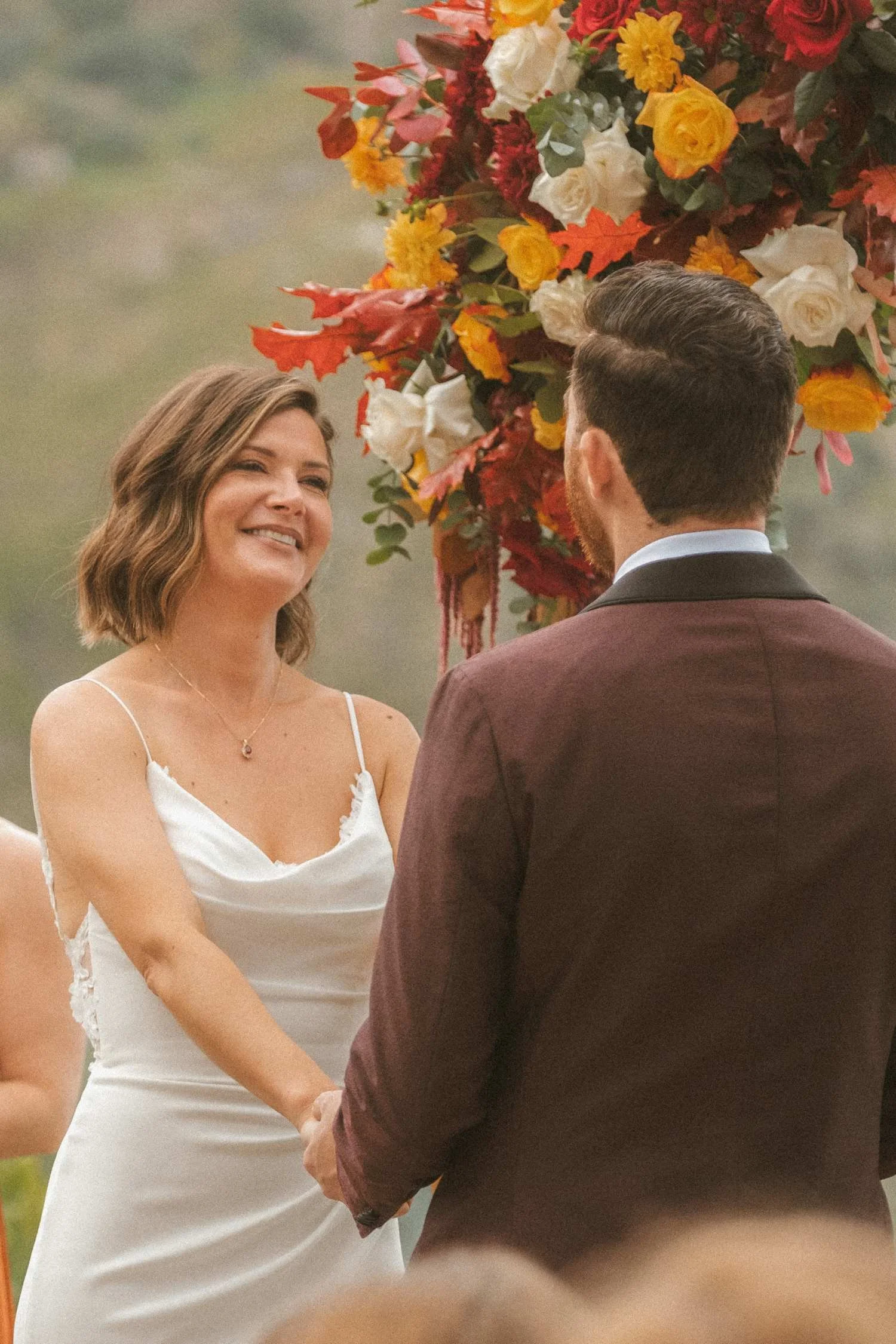 Bride and groom holding hands during outdoor wedding ceremony beneath colorful floral arch