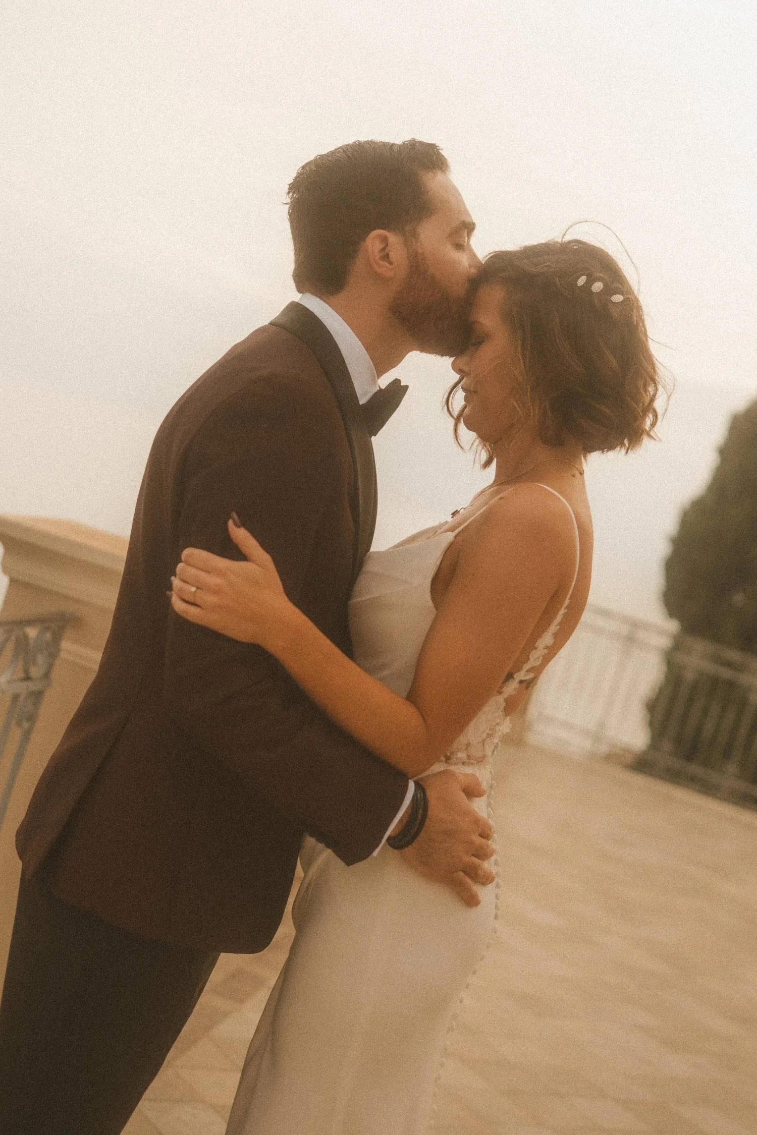 Bride and groom sharing an intimate embrace at sunset on an outdoor terrace, captured in warm cinematic light.