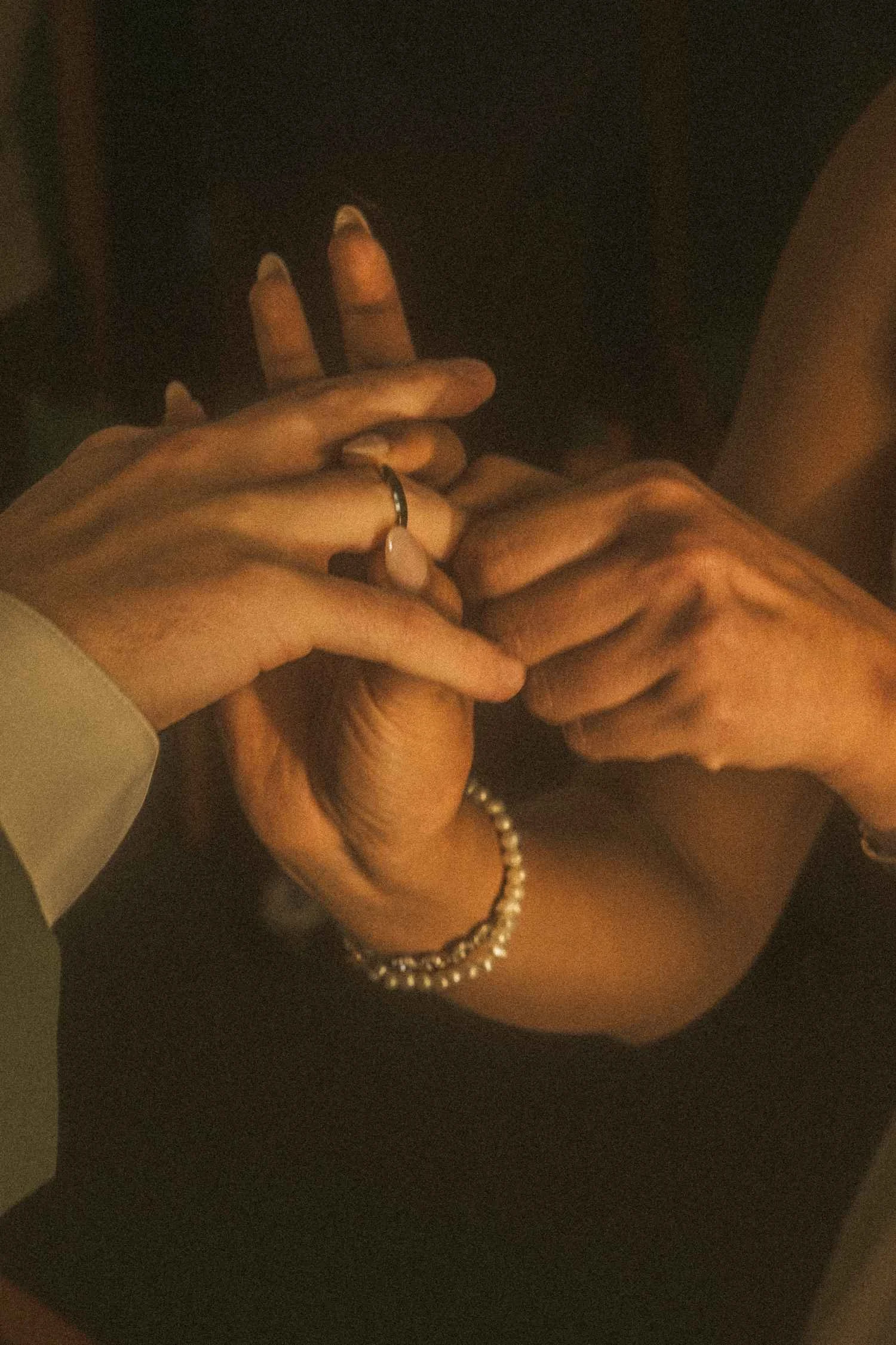 Close-up of hands as a wedding ring is gently placed onto a finger, captured in warm, intimate light.