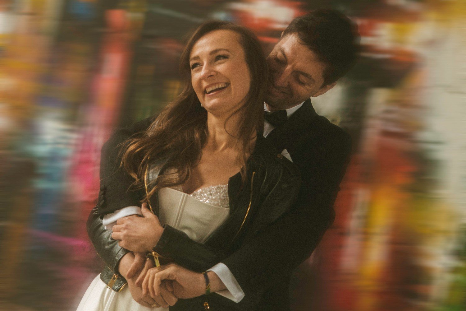 Bride and groom laughing in embrace with colorful graffiti background during wedding photoshoot at Teufelsberg Berlin