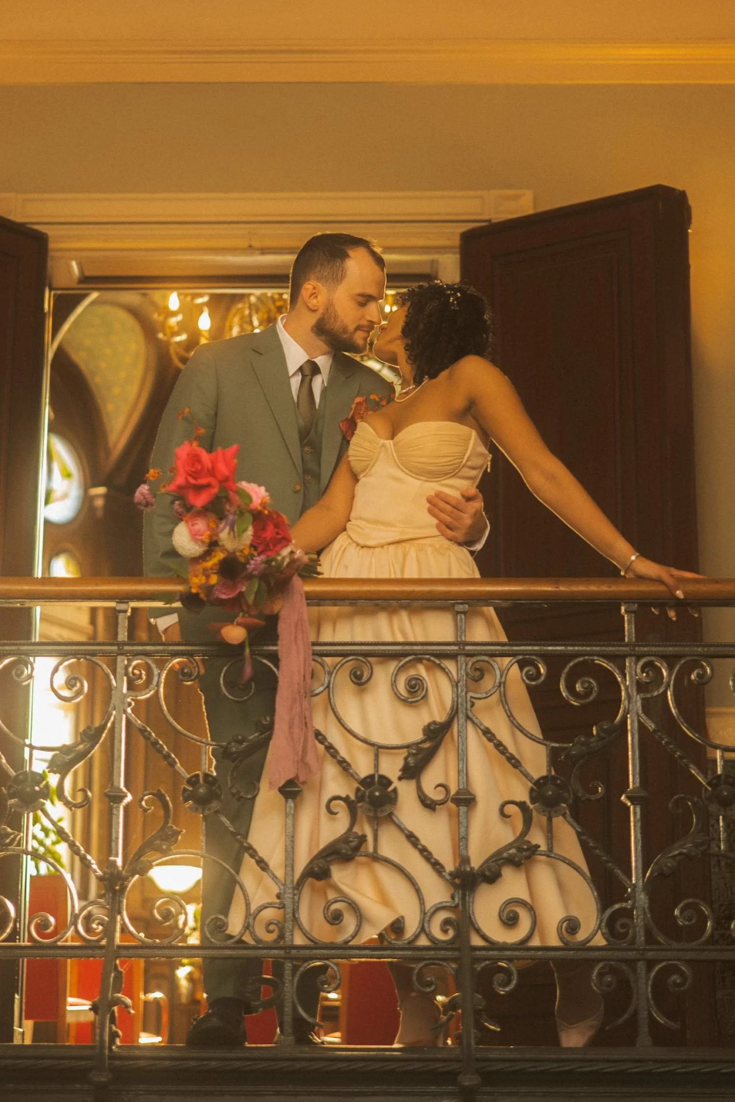 Bride and groom leaning into each other on an indoor balcony, sharing an intimate moment in warm ambient light.