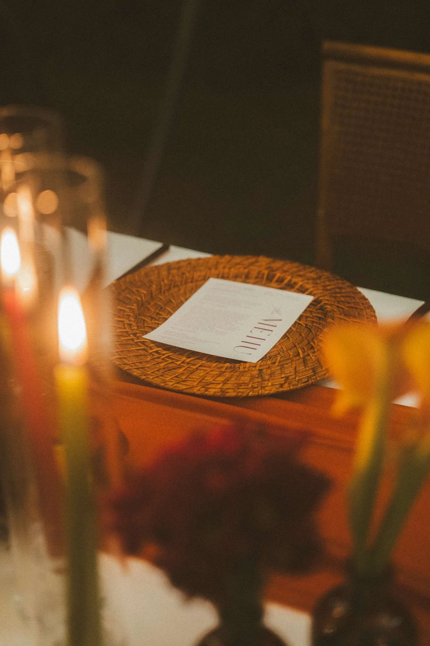 Wedding reception place setting with menu card on woven charger and candles in warm light