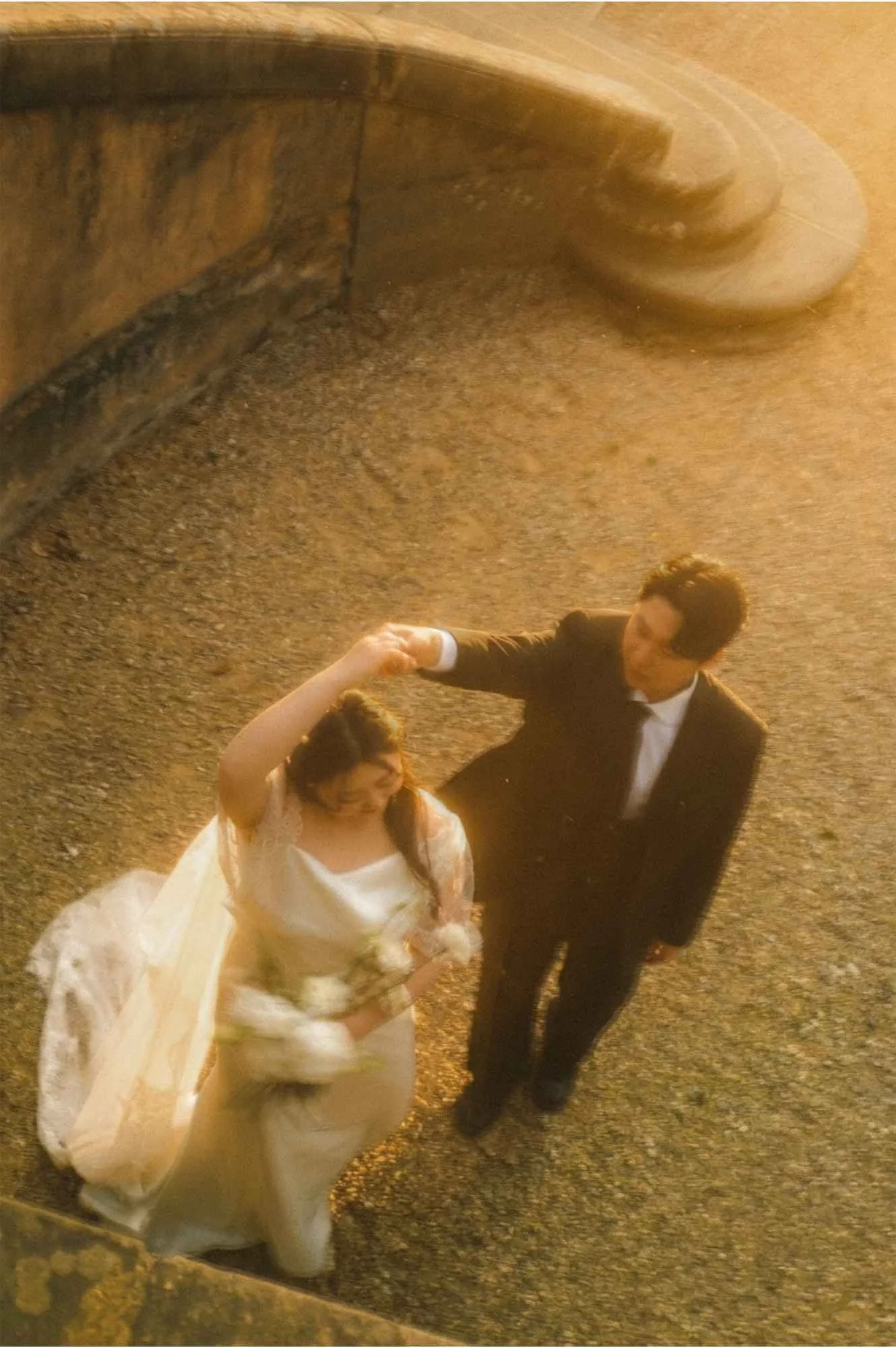 High angle shot of a groom twirling a bride in a white dress and veil on a gravel path during golden hour in Potsdam.