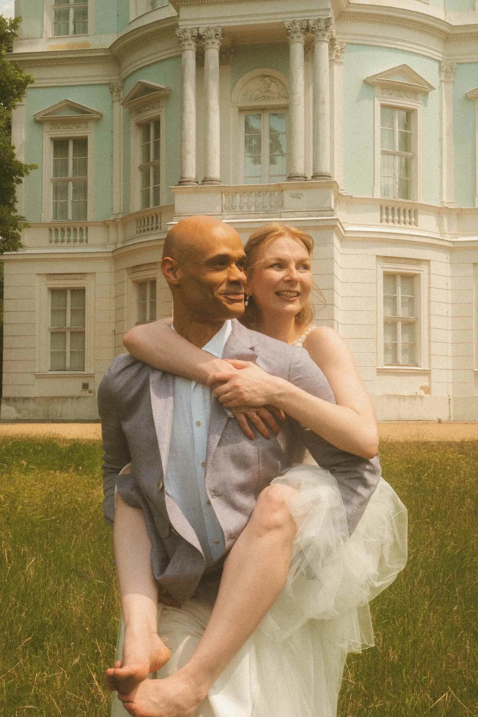Groom carrying laughing bride on his back in front of Charlottenburg Belvedere pavilion, Berlin